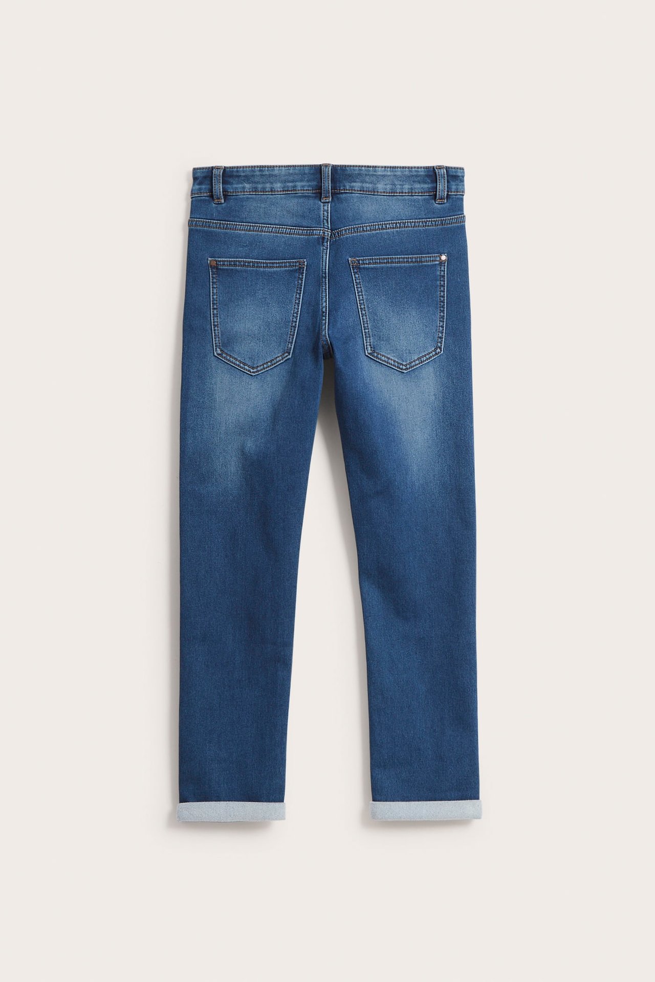 Bakfra av barnas avslappede blå denim joggerjeans med oppbrettede benkanter og to baklommer.