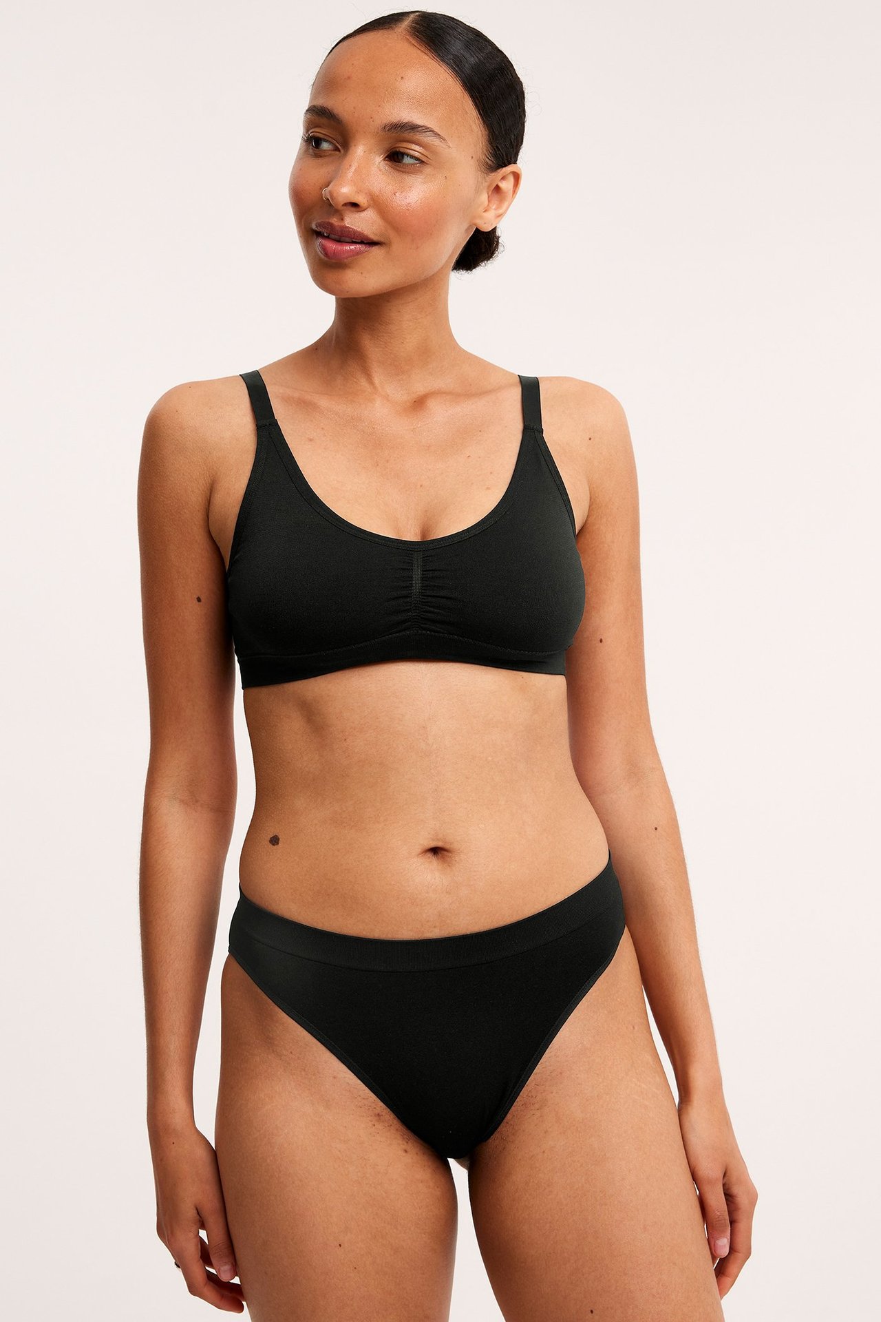 Frontbilde av en kvinne i svart myk truse med ribbet midje og matchende svart myk BH.