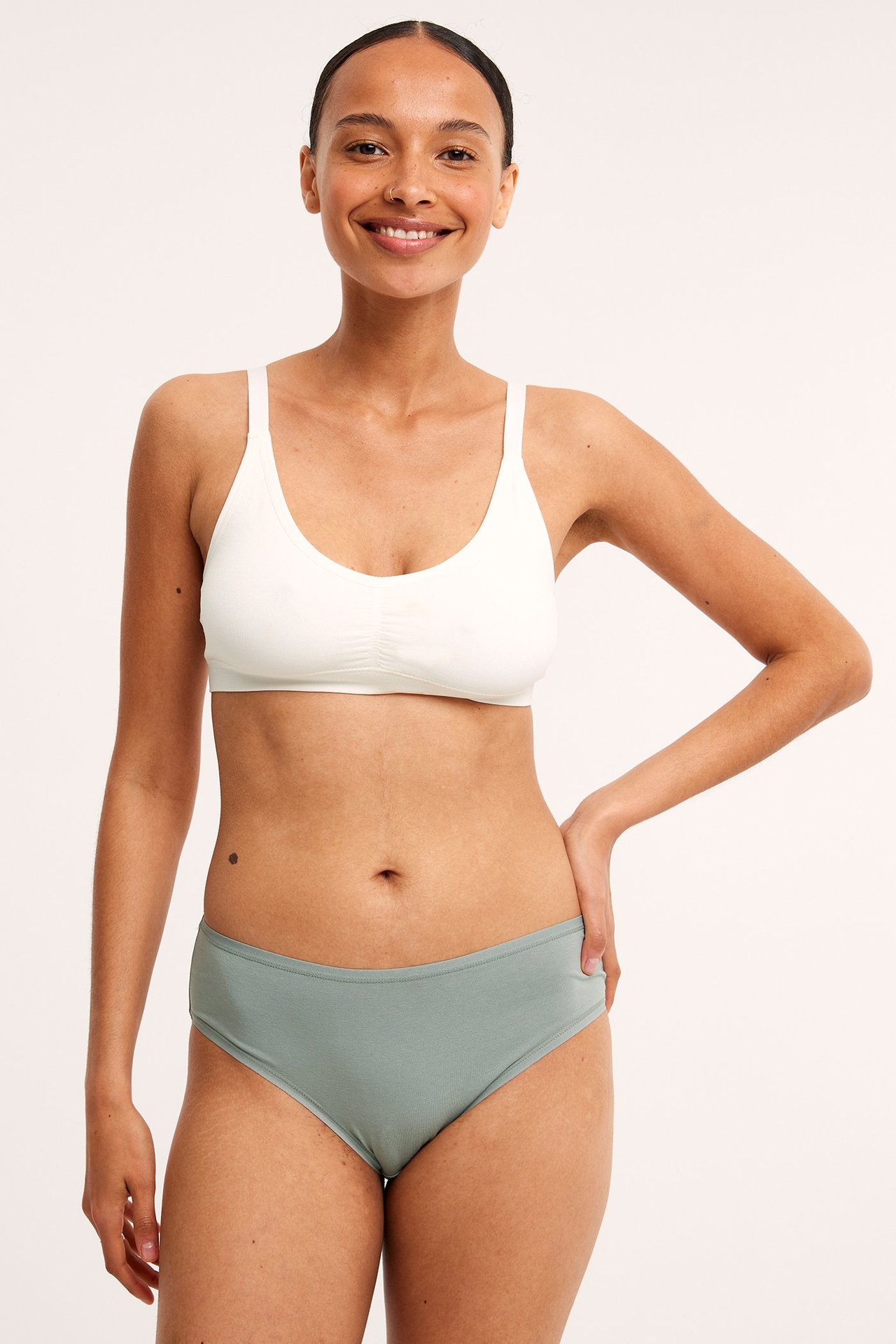 Frontvy av en kvinna i ljusgröna bomullstrosor och en vit bomulls-bh.