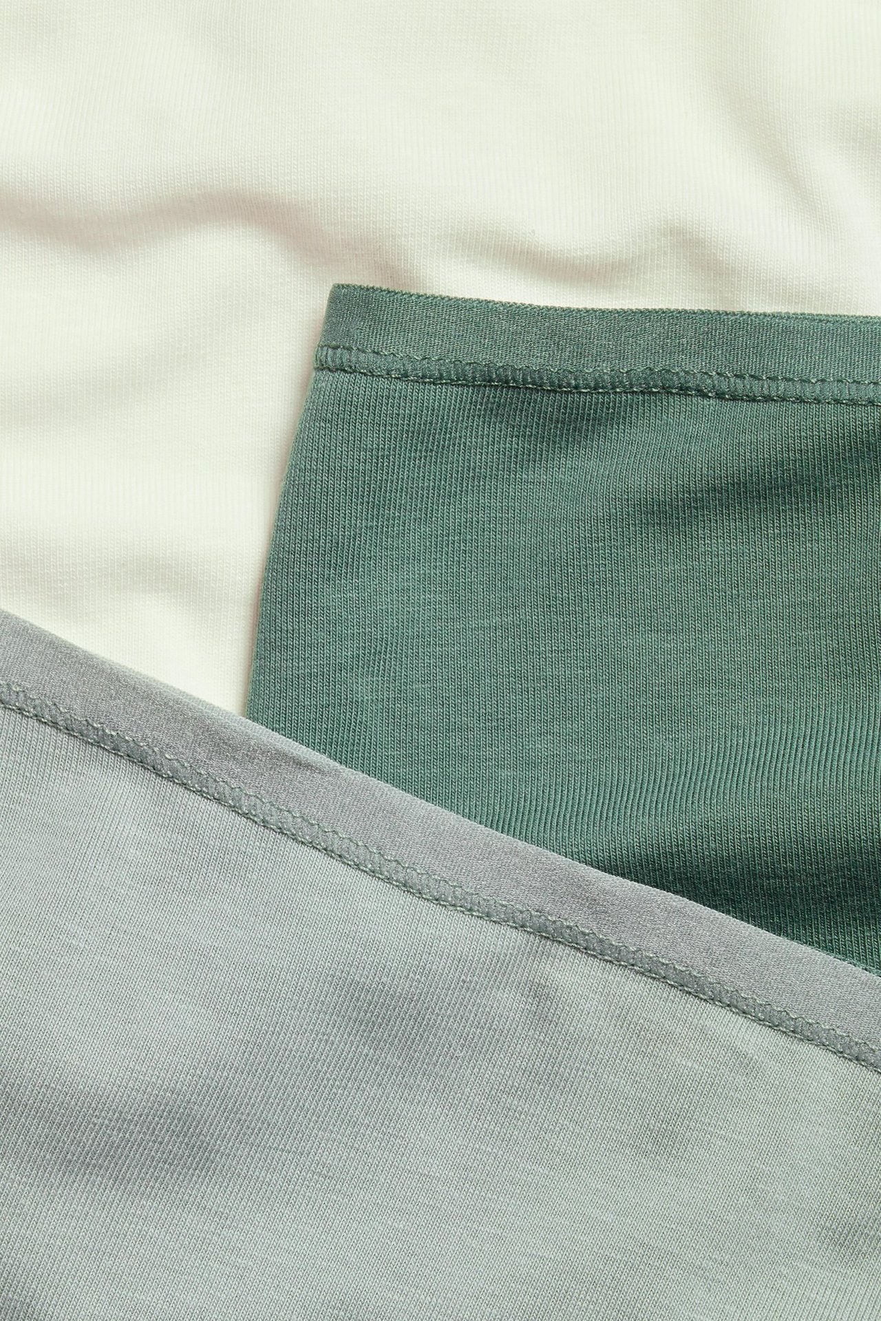 Zbliżenie na trzy jednokolorowe bawełniane figi w jasnej zieleni, ciemnej zieleni i stonowanej zieleni.