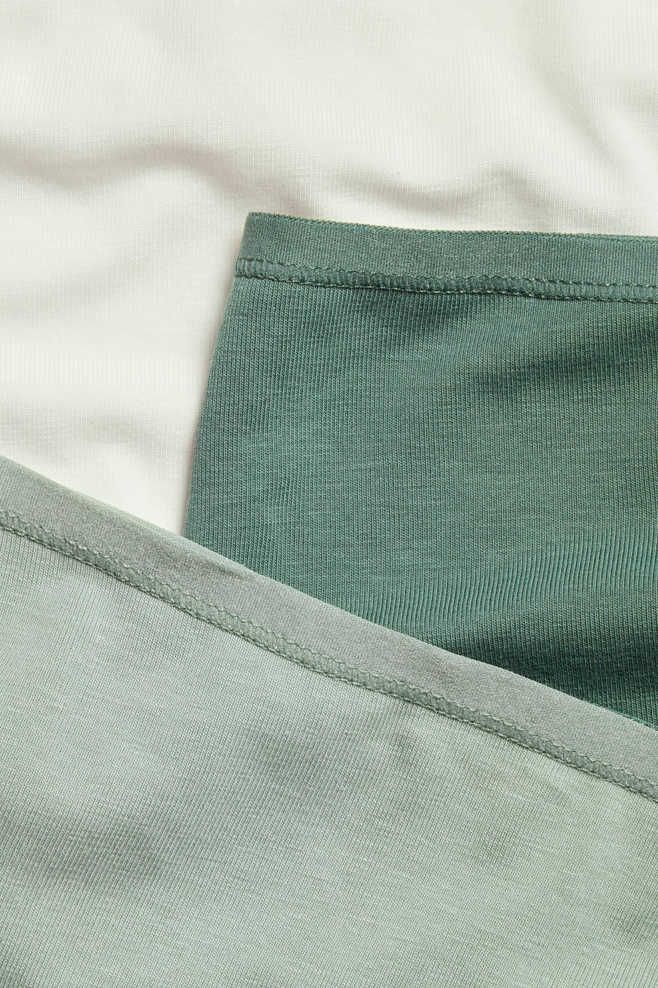 Nærbilde av tre bomullstruser i off-white, mellomgrønt og lysgrønt, med ribbestrikkede og glatte teksturer.