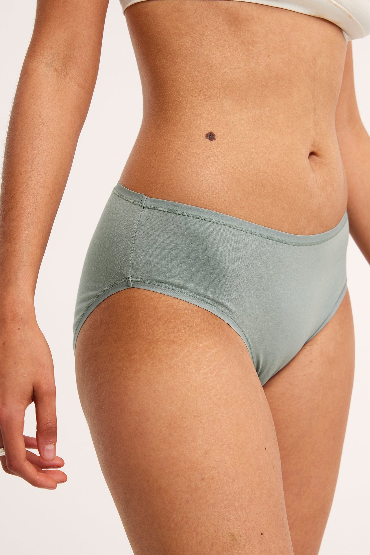 Zbliżenie, widok z boku kobiety w jasnozielonych bawełnianych majtkach i białym biustonoszu.