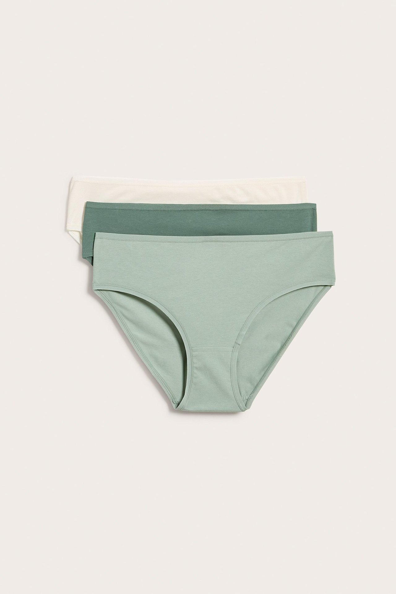 Forfra, tre stablede ensfargede bomullstruser for dame i lys grønn, mørk grønn og eggehvit.