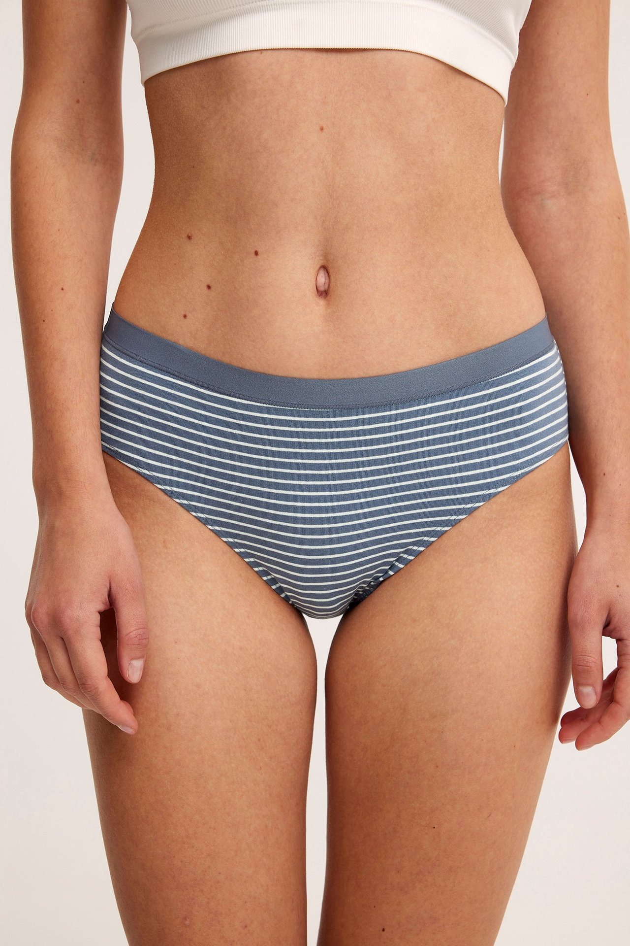 Framifrån, kvinna i blåvitrandiga trosor med normal midja och en vit bralette.