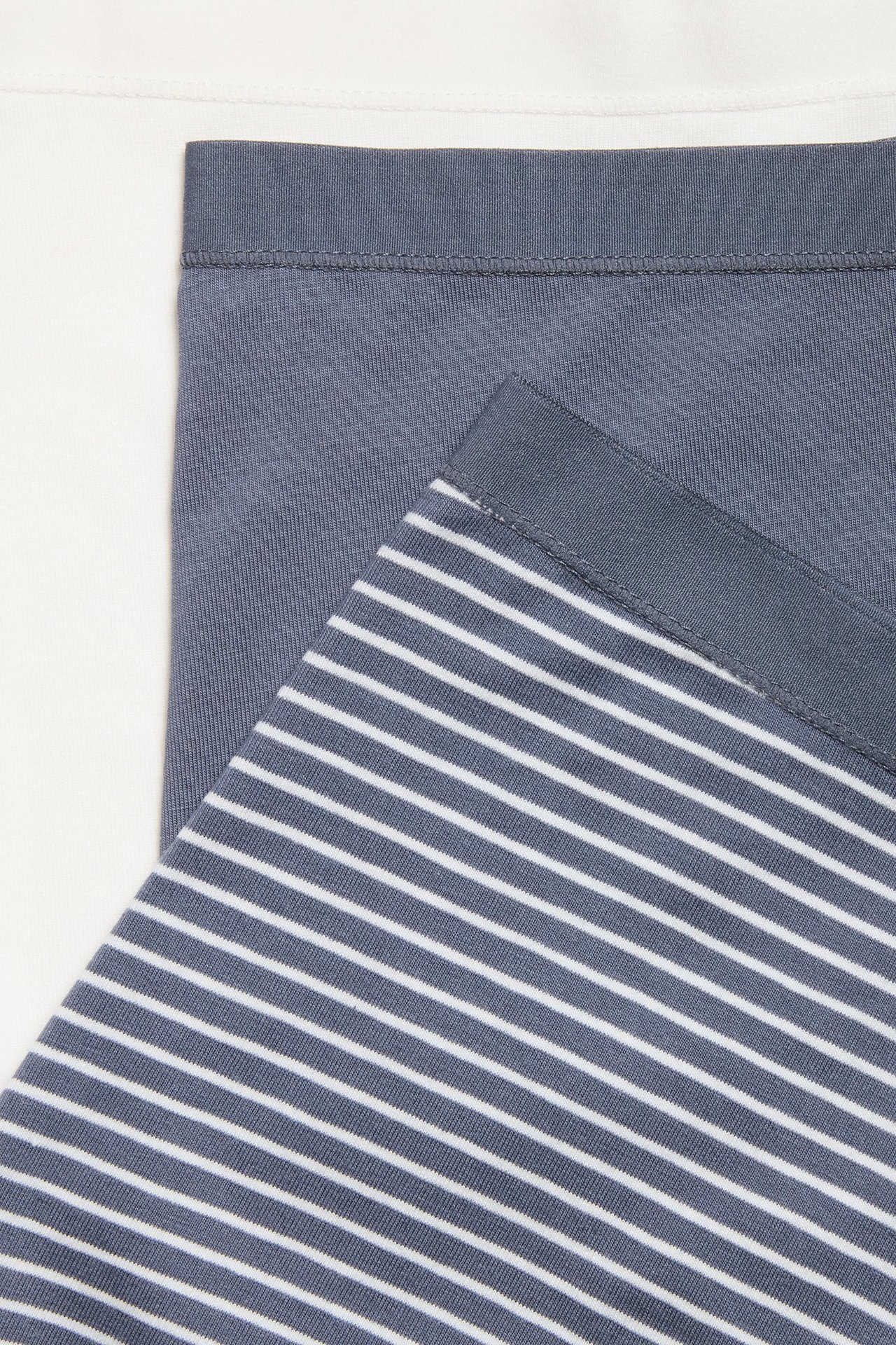 Zbliżenie na trzy złożone damskie bokserki: szare w paski, jednolicie szare i białe.