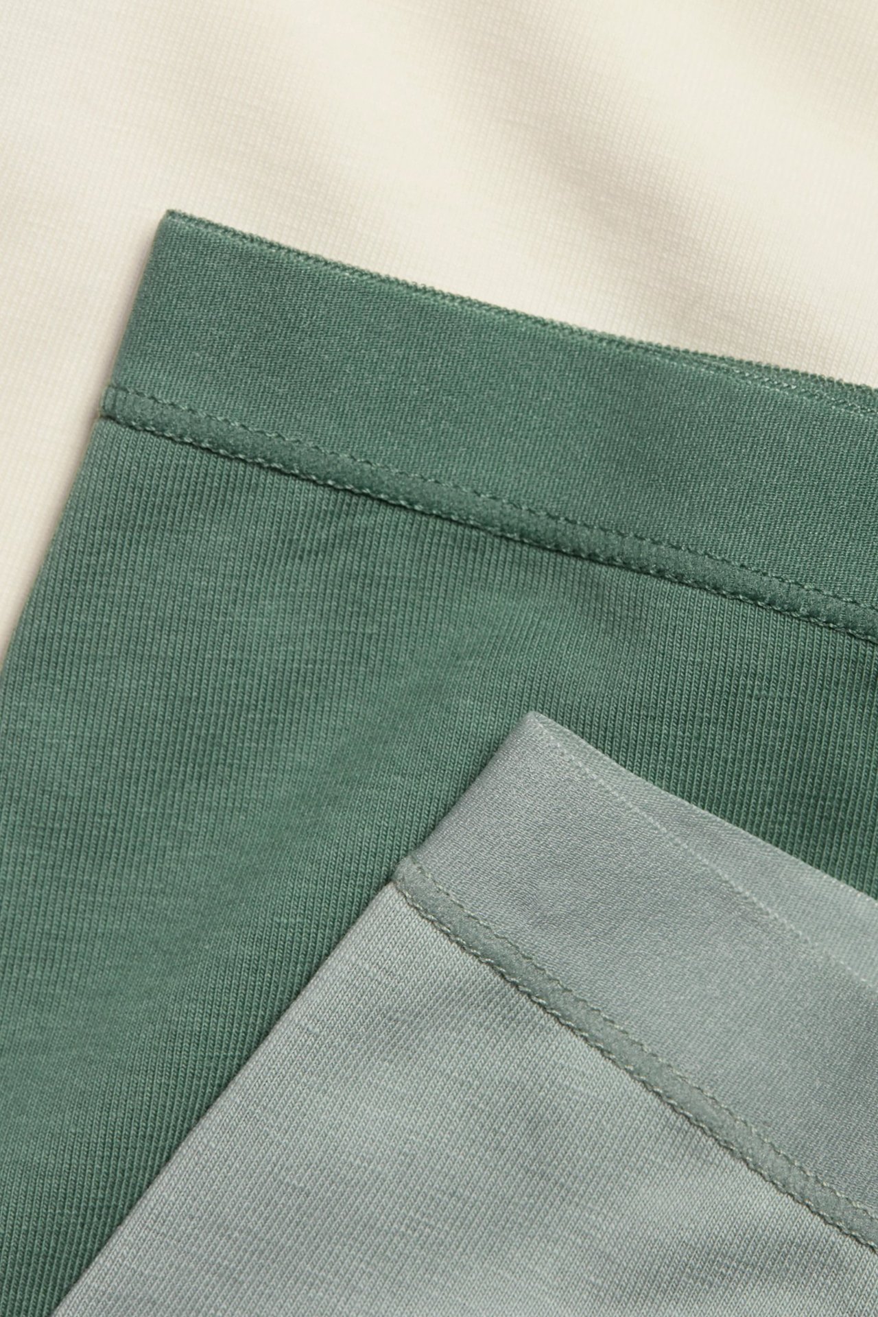 Zbliżenie trzech bawełnianych bokserek w kolorach kremowym, ciemnozielonym i jasnozielonym.