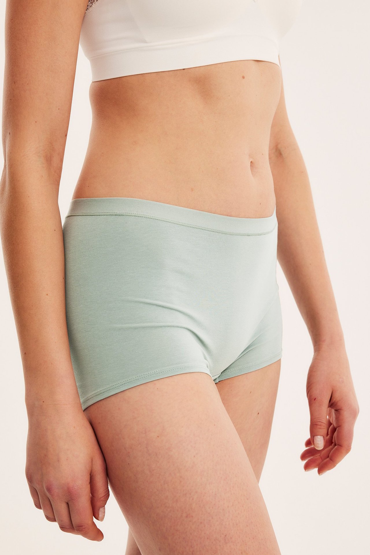 Widok z boku kobiety w jasnozielonych bawełnianych bokserkach i białej braletce.