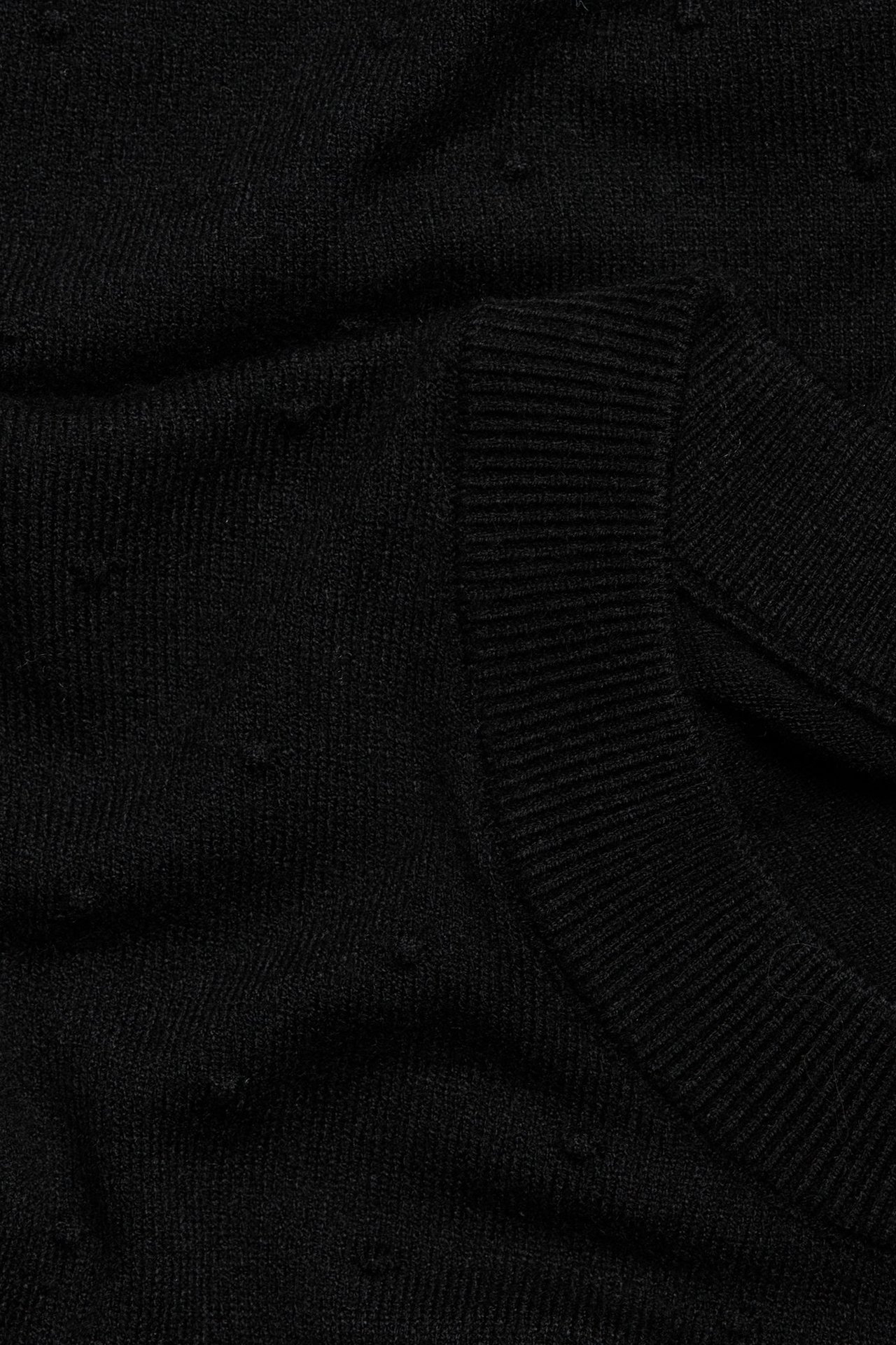 Zbliżenie czarnego dzianinowego swetra ze strukturalnym wzorem w kropki i prążkowanym dekoltem.