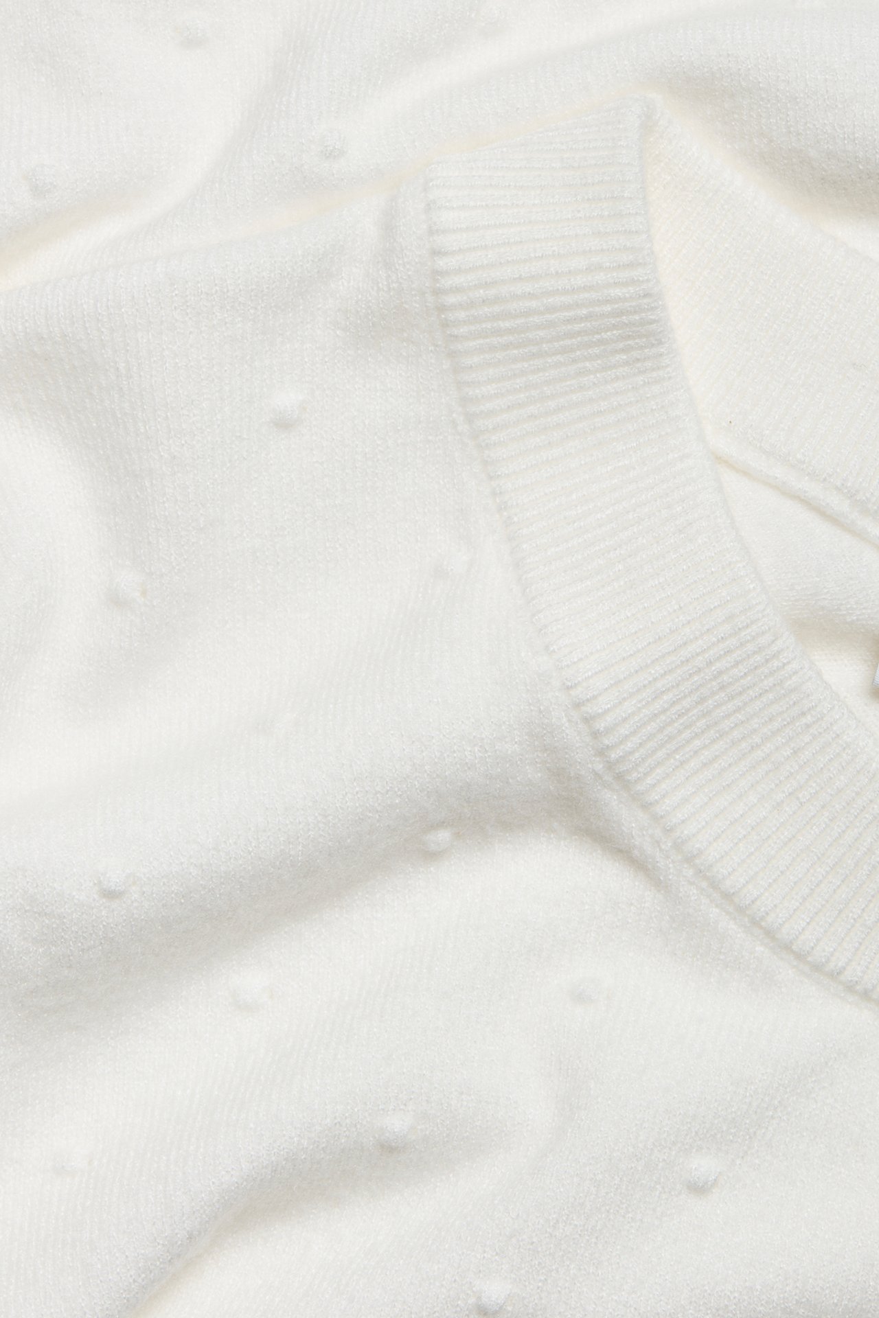 Närbild av en benvit stickad pullover med diskret prickig struktur och ribbad kant.