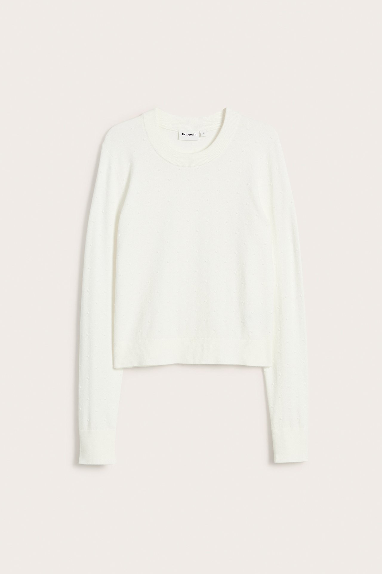 Framifrån, en offwhite stickad kort tröja med diskret prickigt mönster.