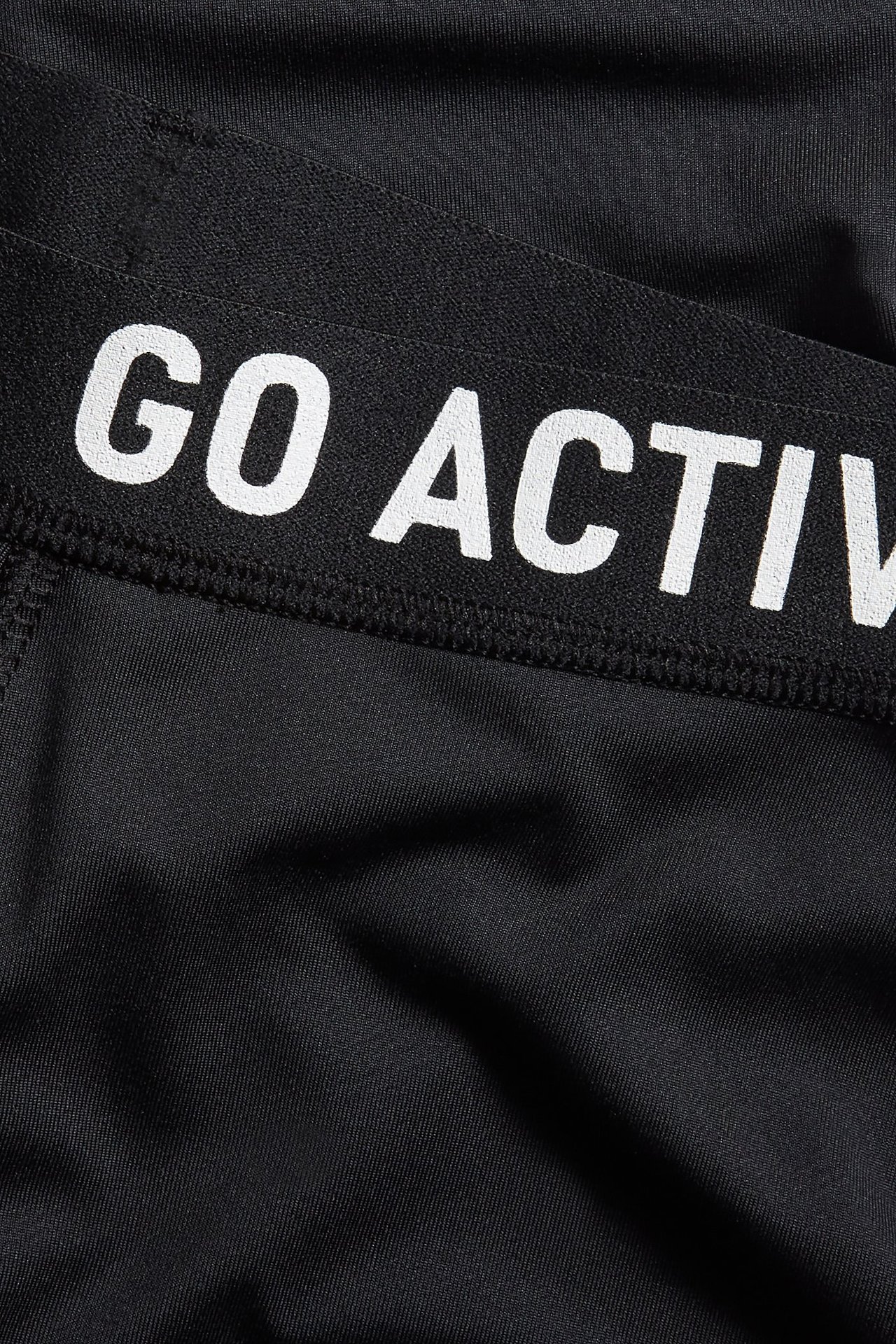 Lähikuva mustista treenitrikoista, joissa on joustava vyötärönauha ja valkoinen "GO ACTIV" -teksti.