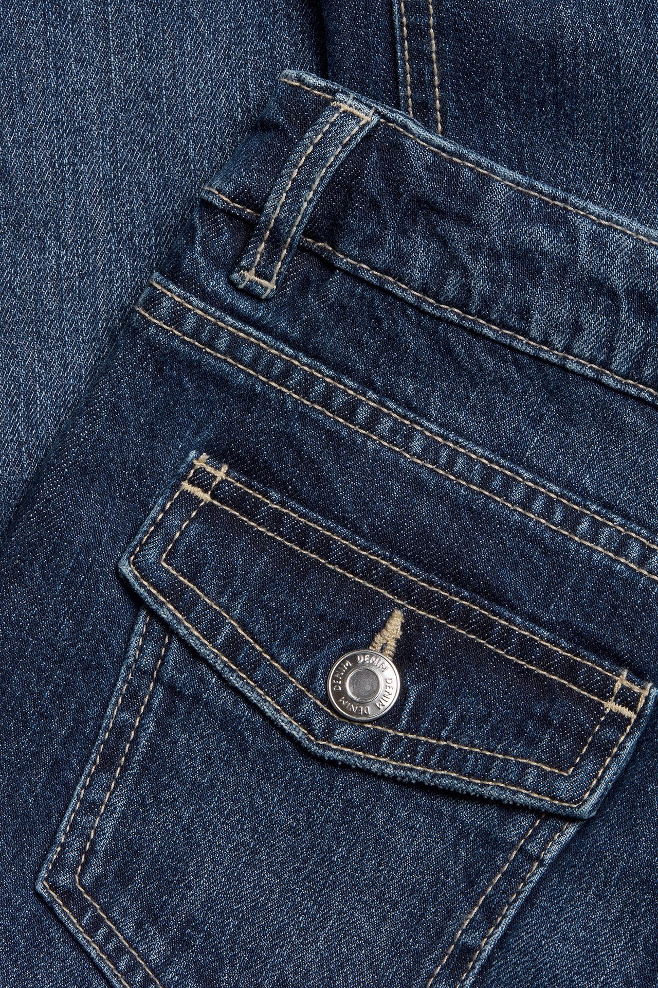 Zbliżenie na ciemnoniebieskie jeansy bootcut z denimu z tylną kieszenią, klapką i srebrnym guzikiem.