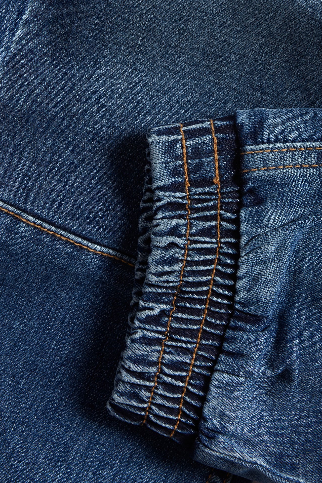 Närbild av blå denim relaxed jeans som visar den elastiska muddkanten med orange sömmar.