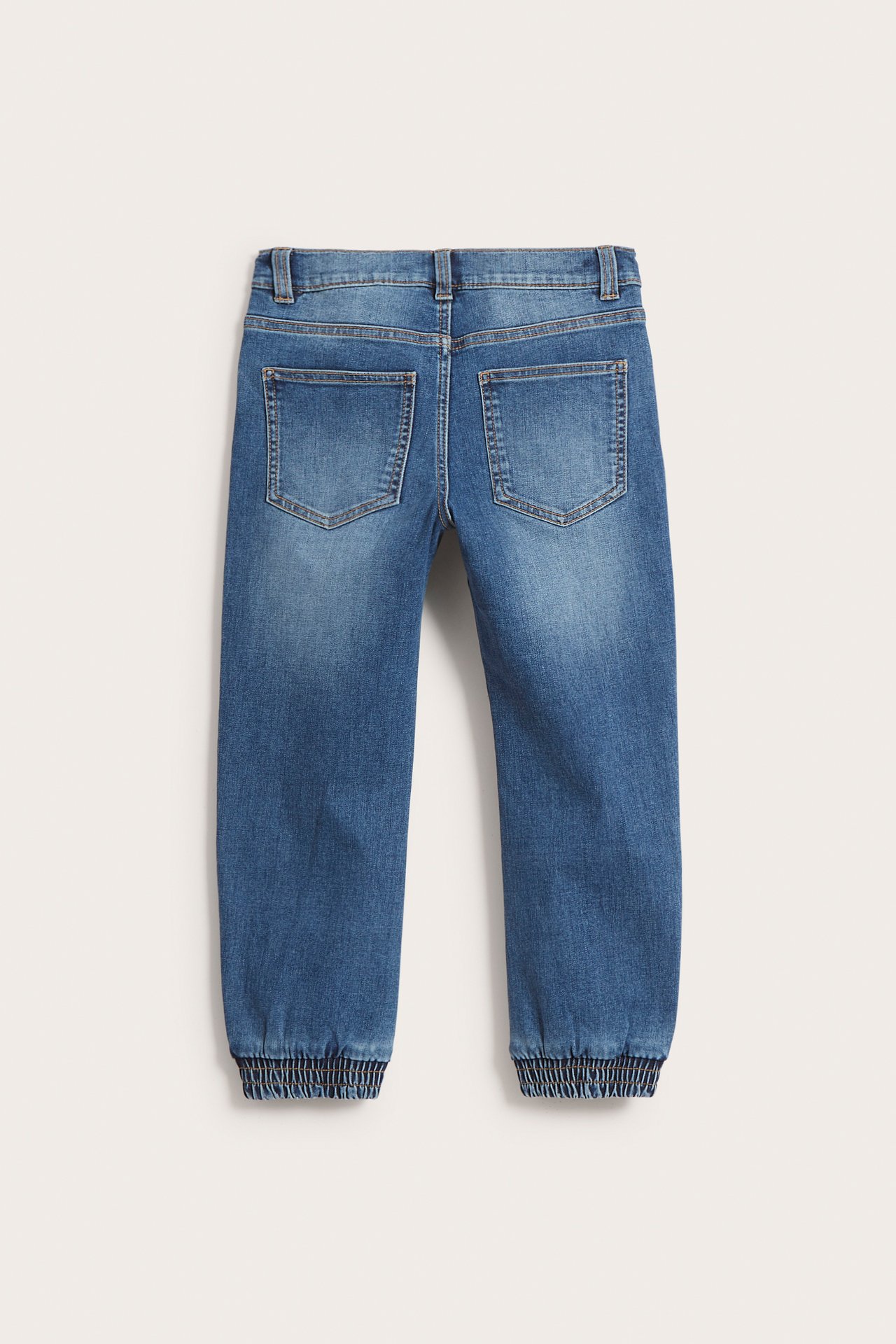 Bakifrån: blåa, avslappnade jeans för barn i denim med resår i benslut och två bakfickor.