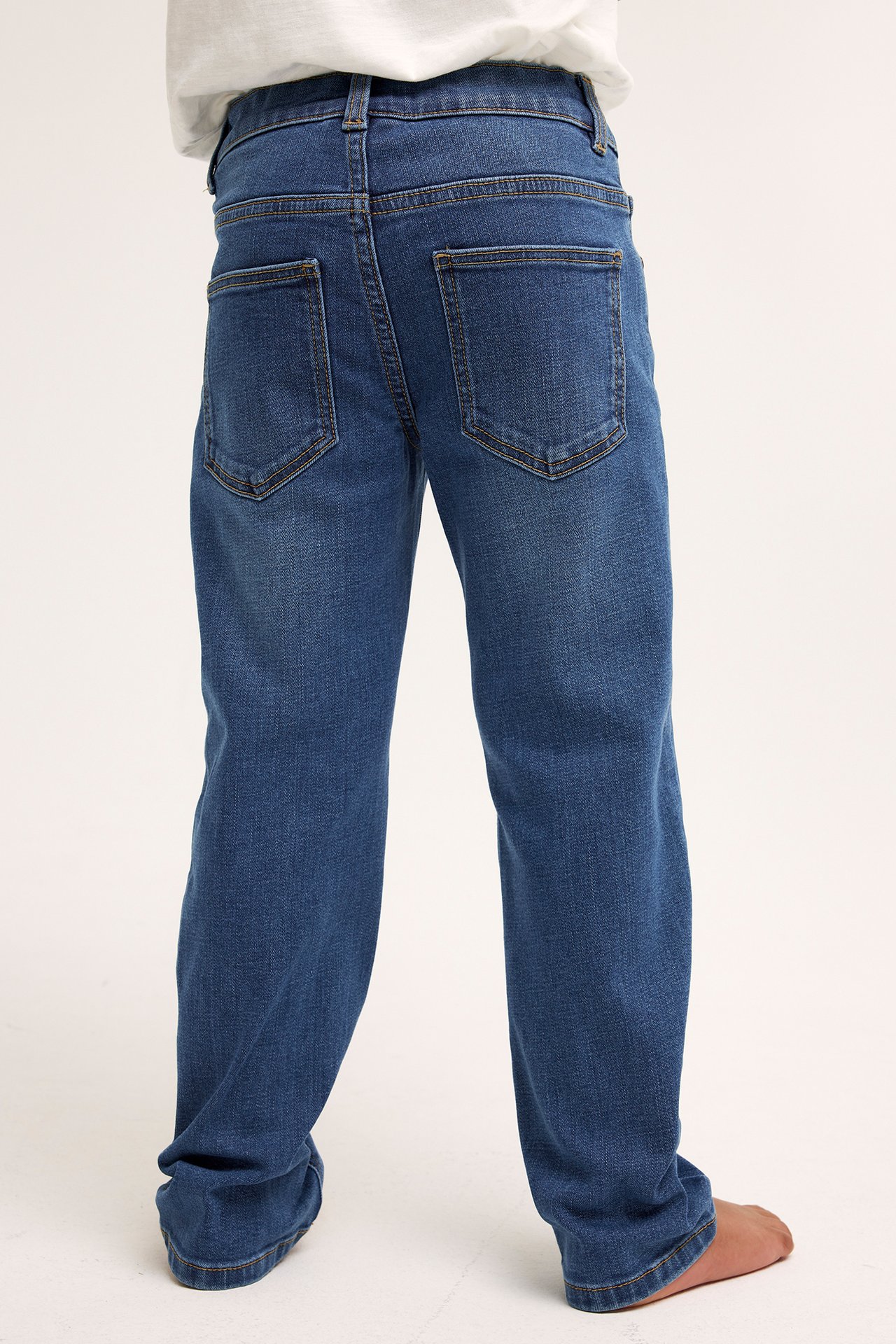 Bakfra, et barn i blå rette denimjeans med baklommer og en hvit t-skjorte.