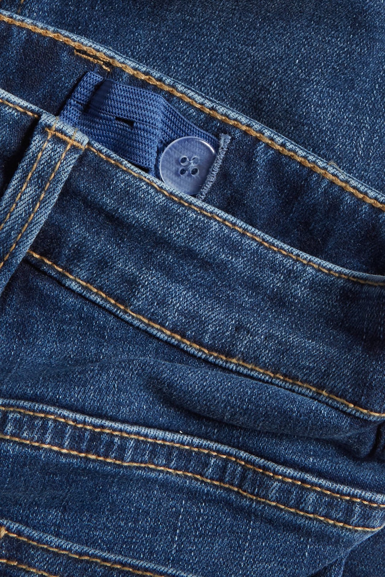 Zbliżenie na niebieskie jeansy denim z regulowaną gumką w pasie i przezroczystym guzikiem.
