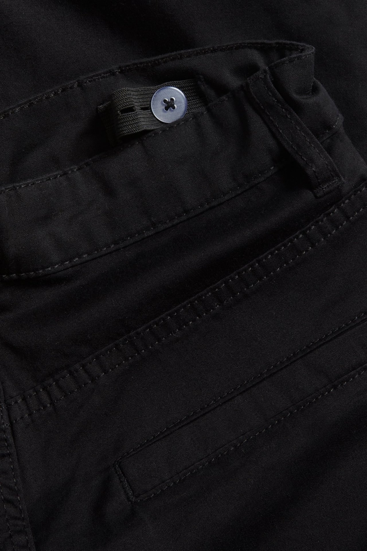 Zbliżenie czarnych spodni cargo dziecięcych, pas z regulowaną gumką i jasnym guzikiem.