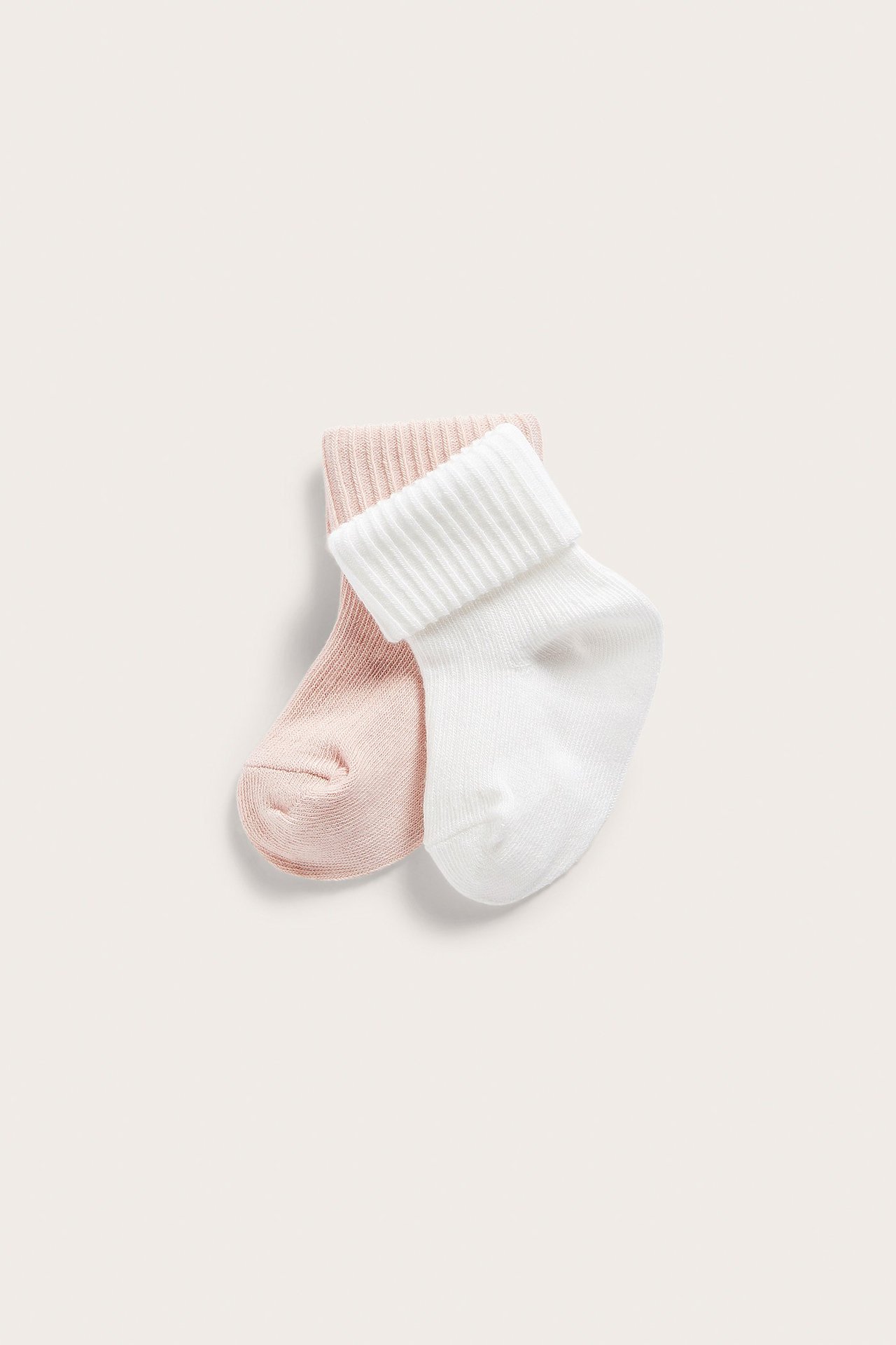 Nærbilde av to ensfargede babystrømper: en lys rosa og en hvit, begge med ribbestrikkede mansjetter.
