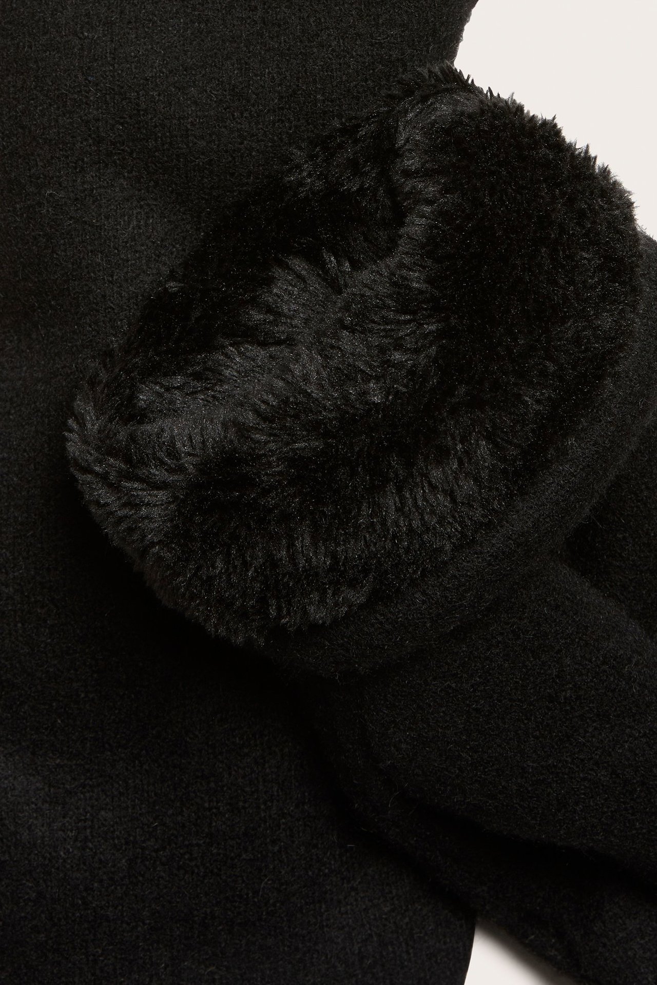Zbliżenie czarnej rękawiczki z wełny z puszystą czarną podszewką z misia widoczną przy mankiecie.