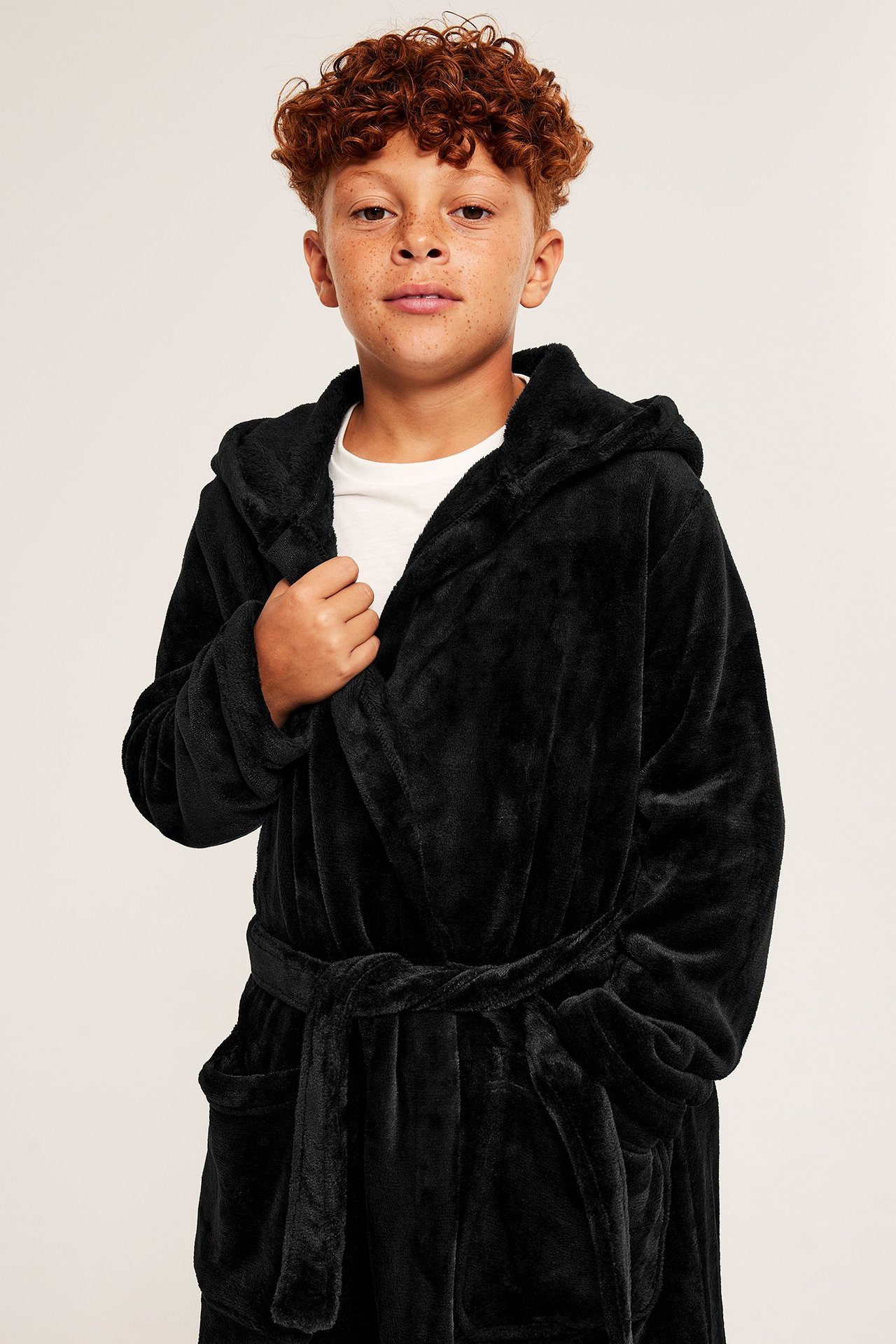 Edestä, lapsi mustassa hupullisessa fleece-kylpytakissa, solmittu vyö, valkoinen t-paita alla.
