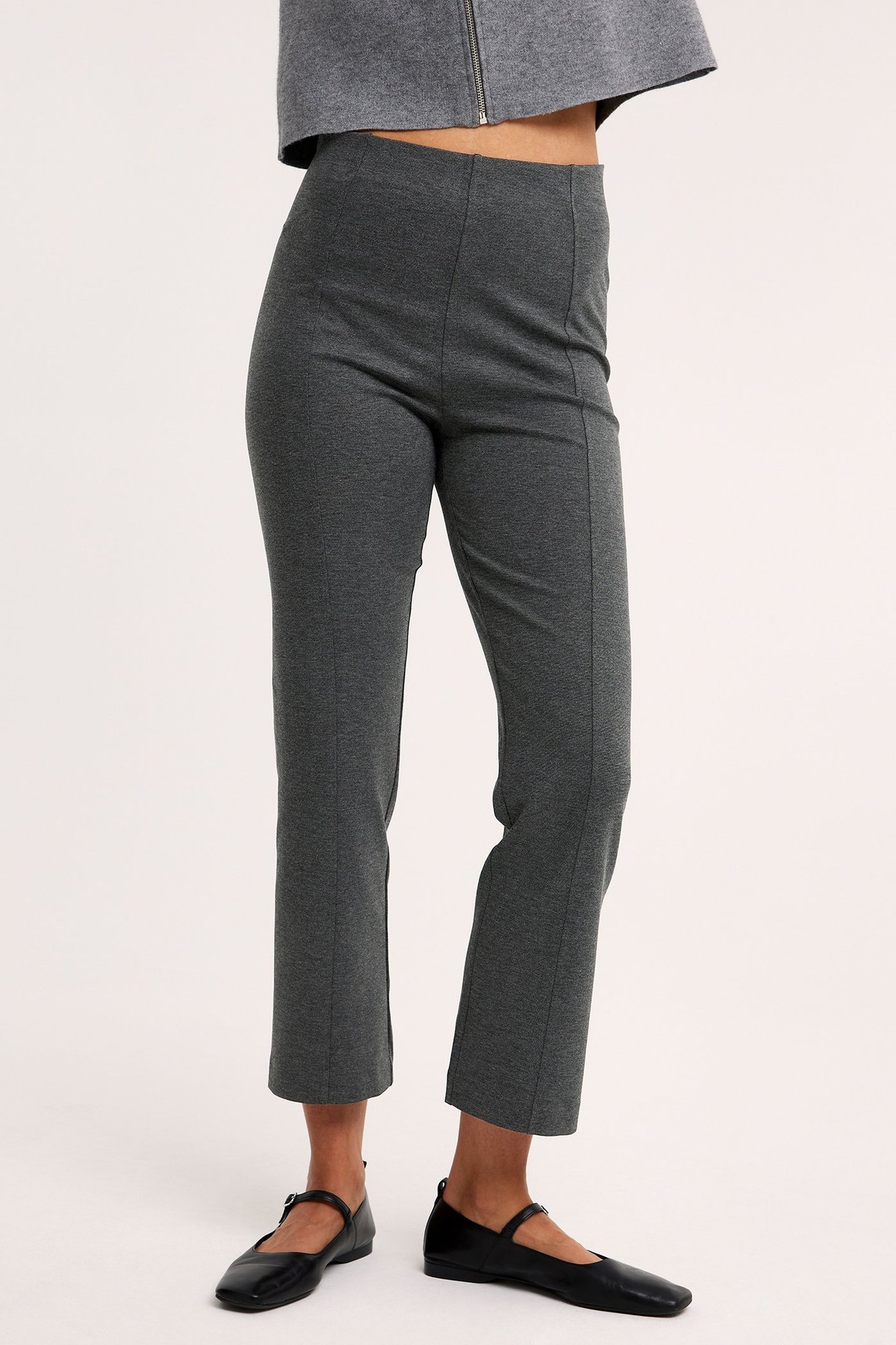 Sidebilde av kvinne i mørkegrå melert kickflare pull-on bukse, grå kort topp og svarte flate sko.
