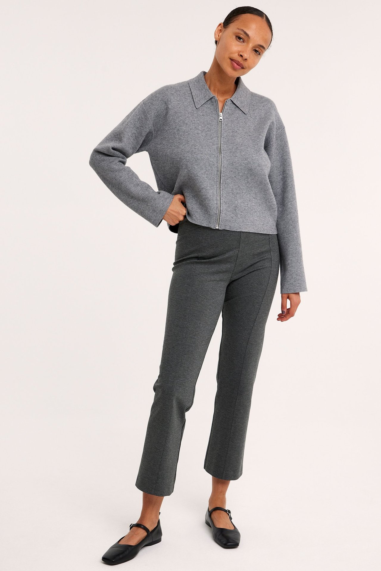 Widok z przodu: kobieta w ciemnoszarych spodniach pull-on kickflare, szarej kurtce na zamek i czarnych butach.