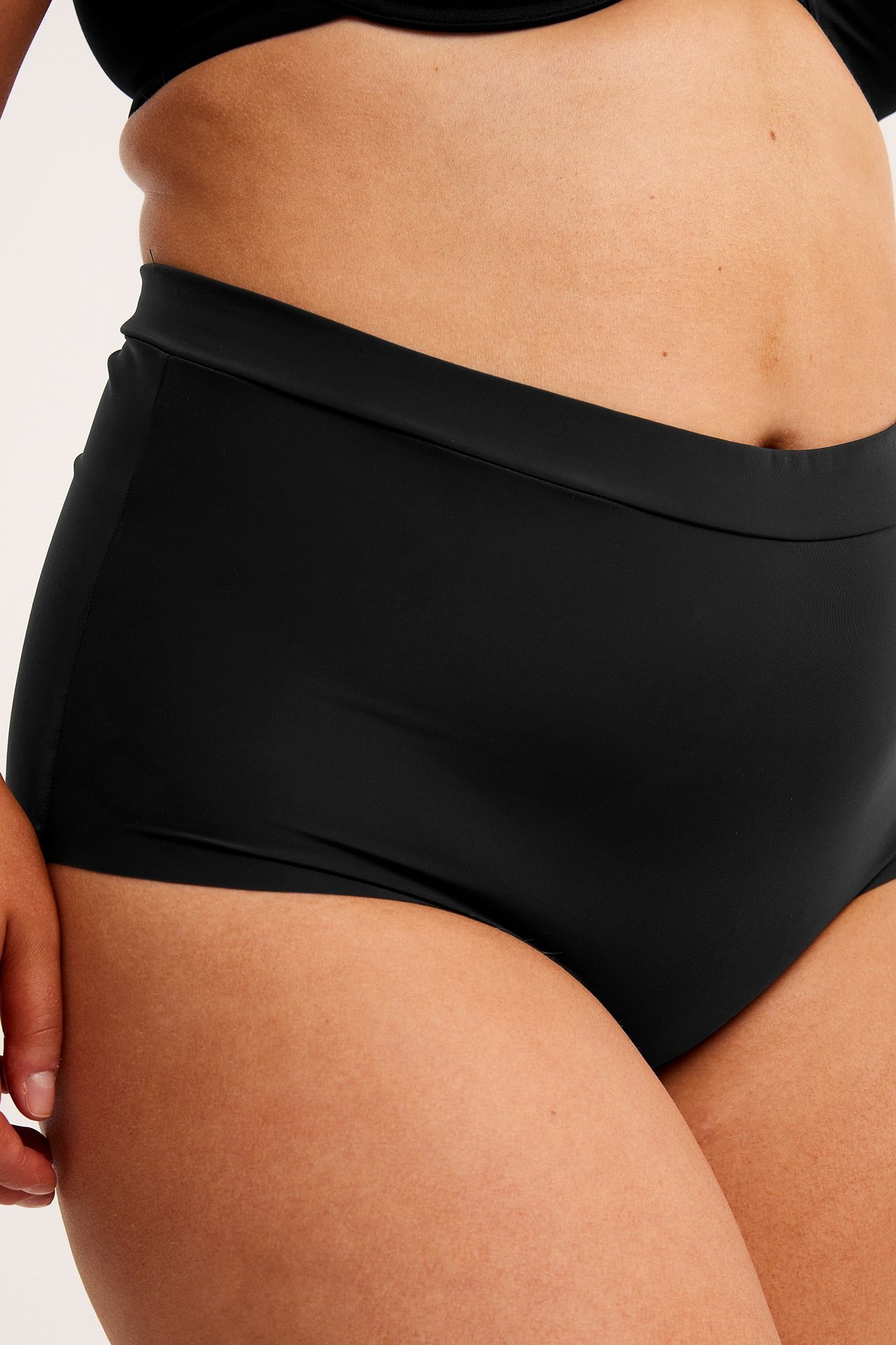 Lähikuva edestä naisesta, jolla on mustat yksiväriset mikro hipster-alushousut leveällä vyötärönauhalla.