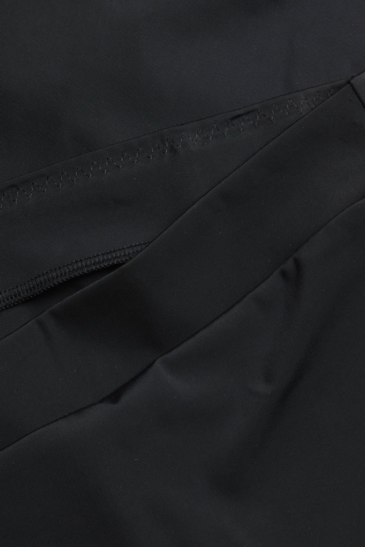 Zbliżenie czarnych fig biodrówek z mikrofibry z elastycznym pasem i zygzakowatym szwem.