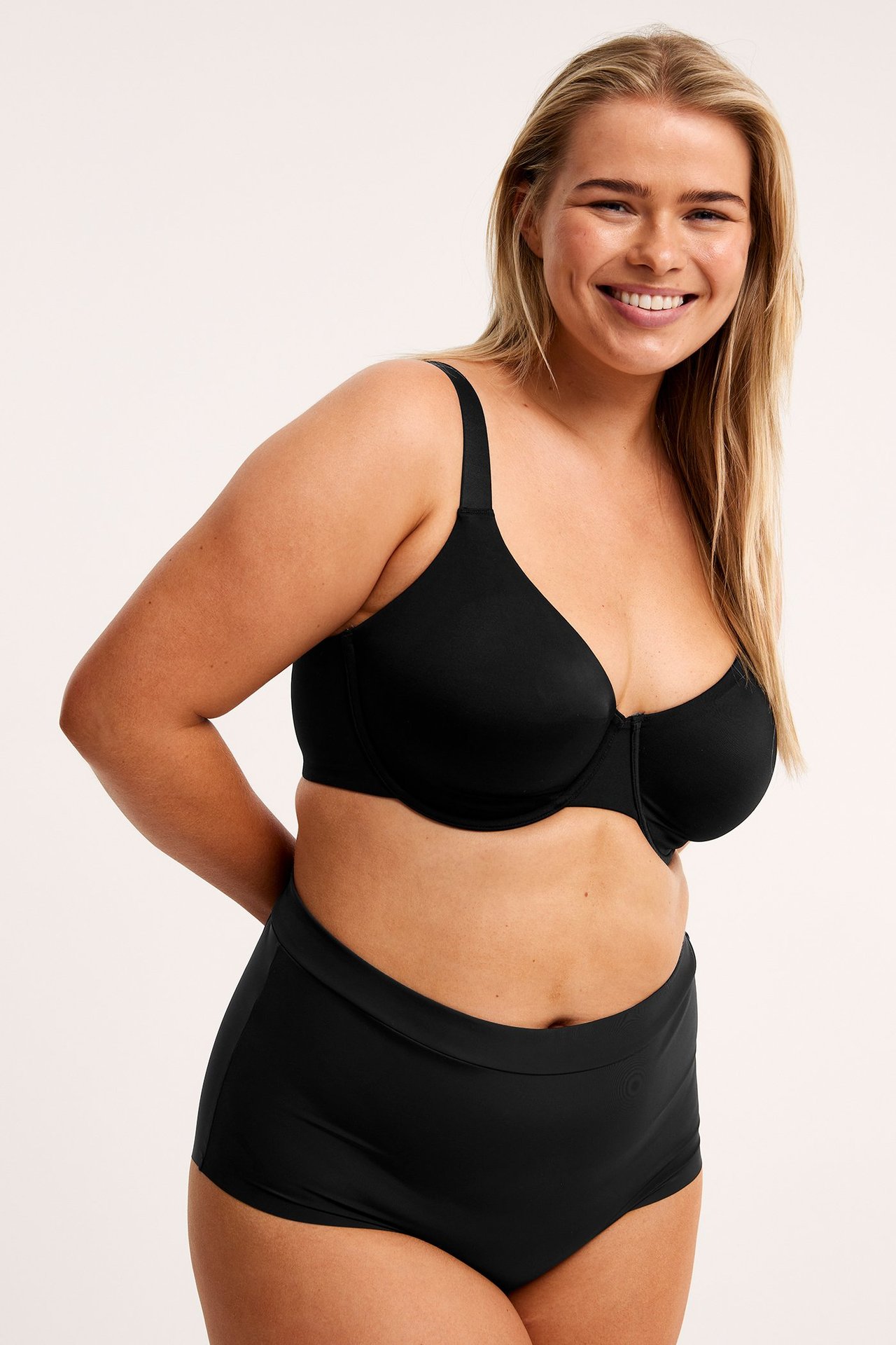 Frontbilde av en kvinne i svarte sømløse mikro hipster-truser og en matchende svart BH.