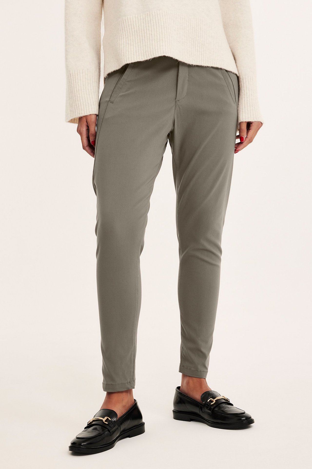 Forfra: kvinne i smale khakifargede boyfriend-bukser, en kremfarget strikkegenser og svarte loafers.