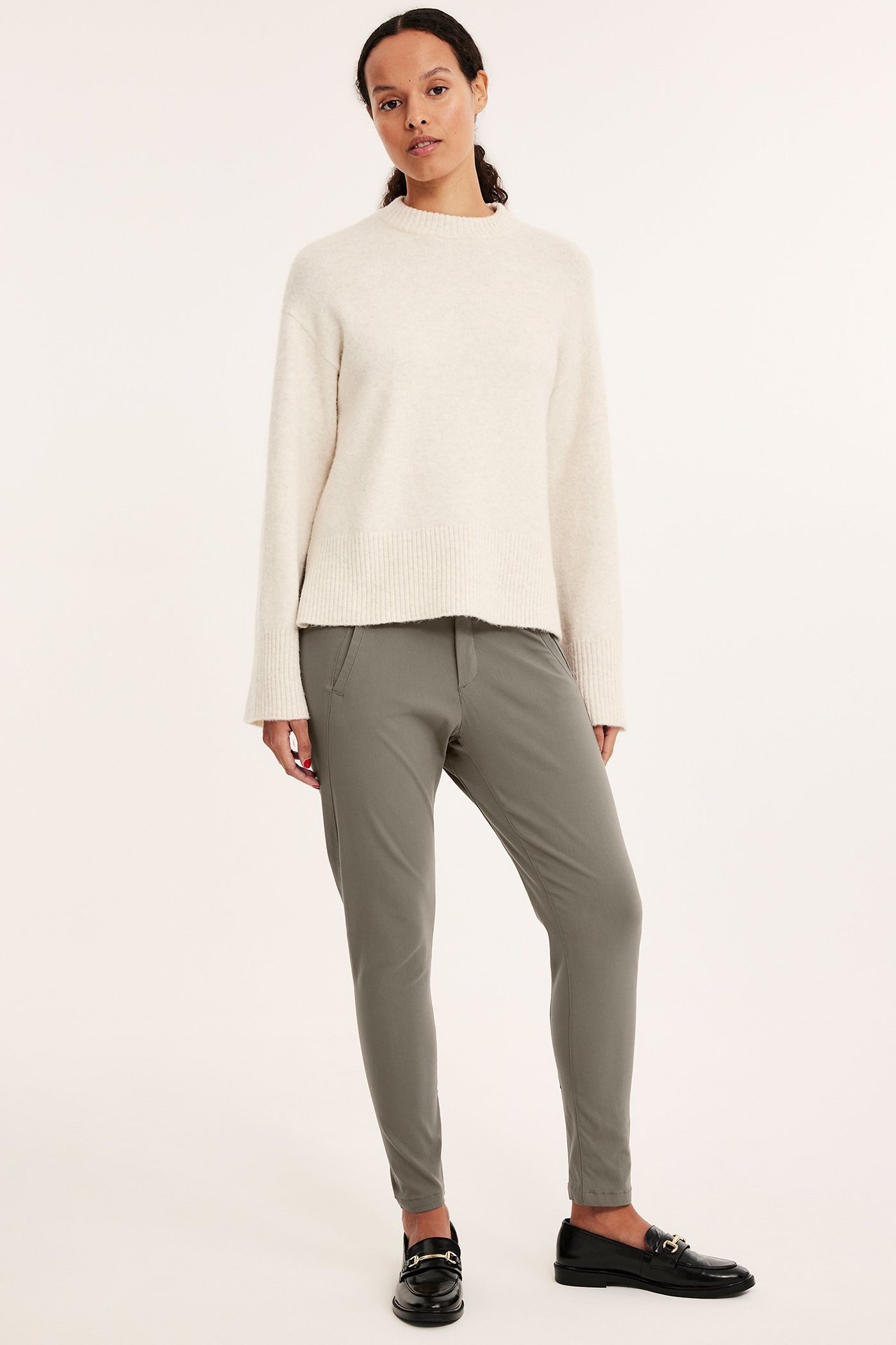 Widok z przodu kobiety w dopasowanych spodniach boyfriend khaki, kremowym swetrze i czarnych mokasynach.