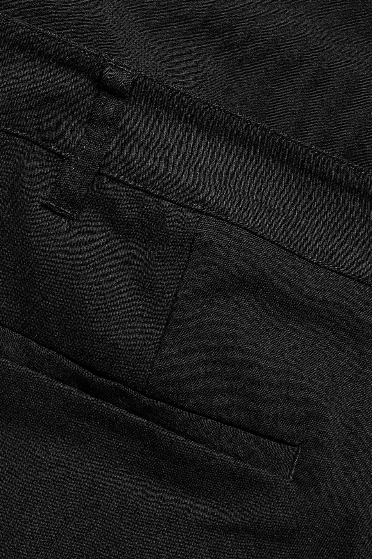 Zbliżenie czarnych damskich spodni garniturowych, pokazujące szlufkę i detal kieszeni.