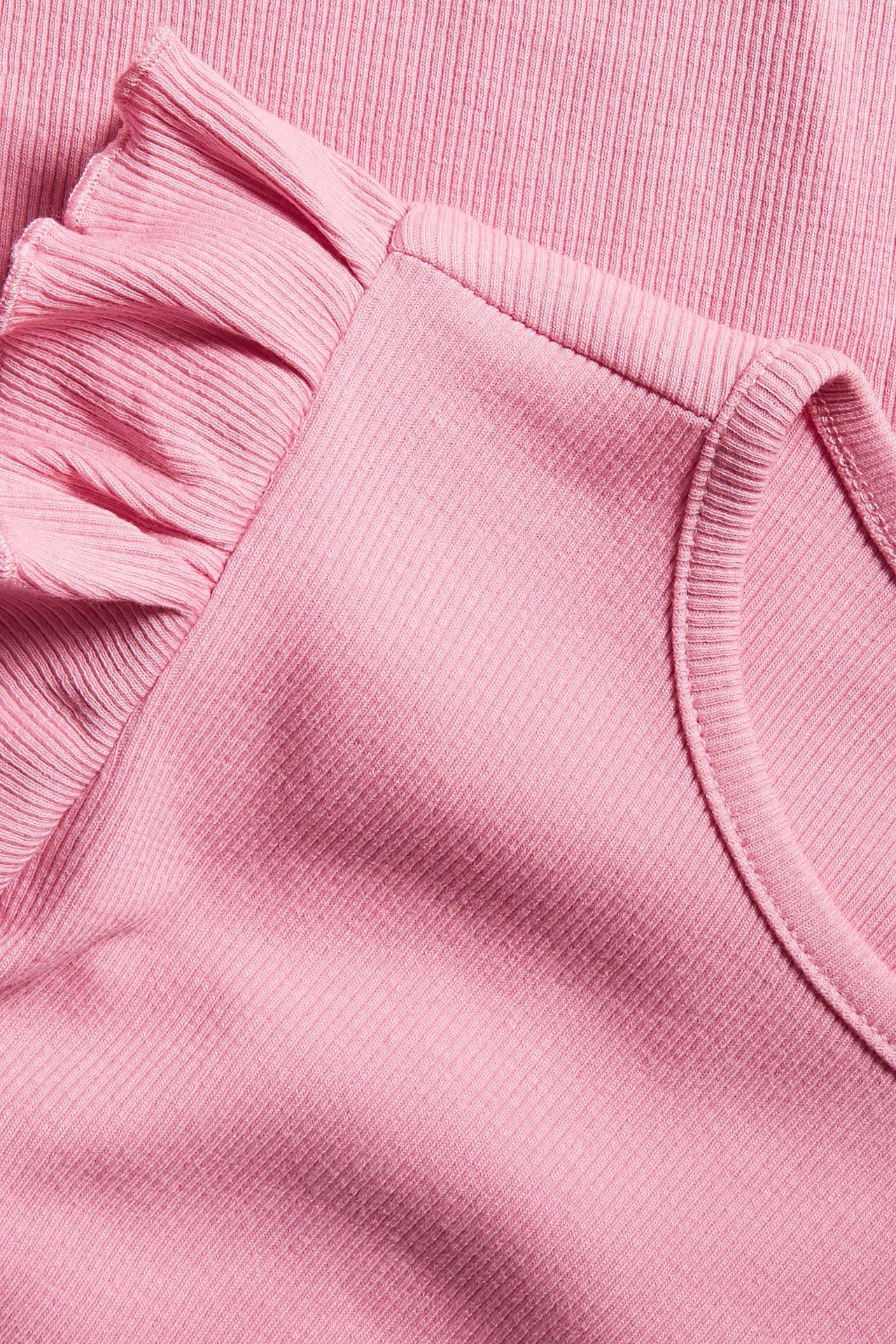 Närbild på en rosa ribbad trikåklänning med volangdetalj på axeln.