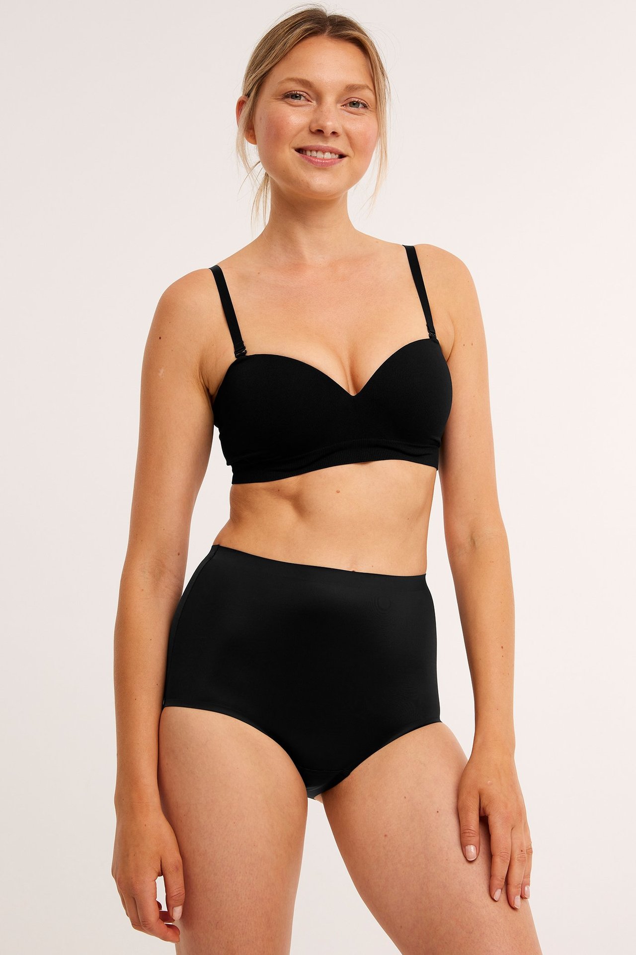 Forfra, kvinne i svarte høytlivs shaping-truser og svart stroppeløs BH.