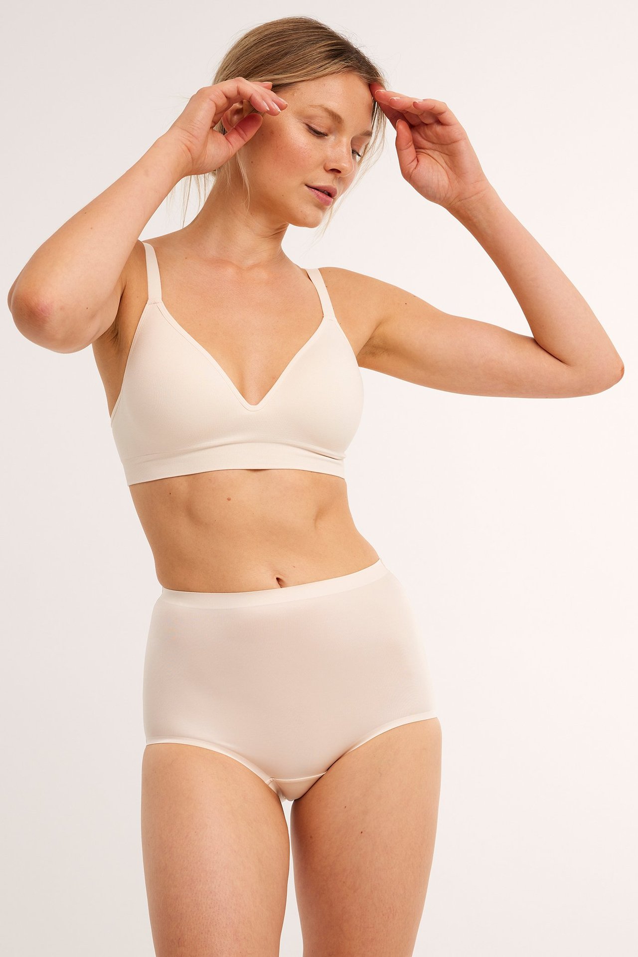 Frontbilde av kvinne i beige høytlivs shapingtruser i satinmicro og matchende BH.