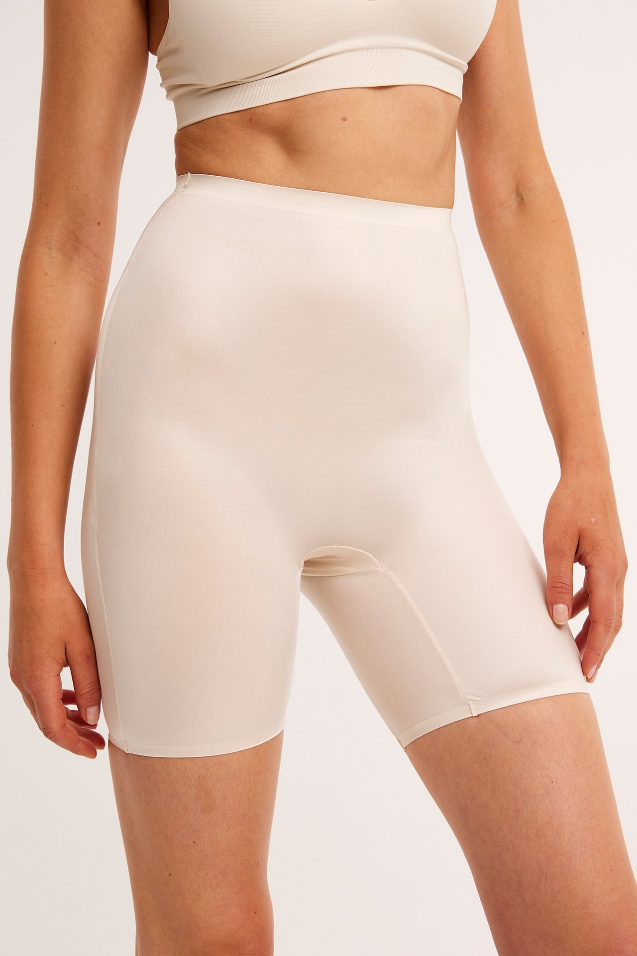 Widok z przodu kobiety w beżowych szortach modelujących z wysokim stanem i pasującym beżowym biustonoszu.