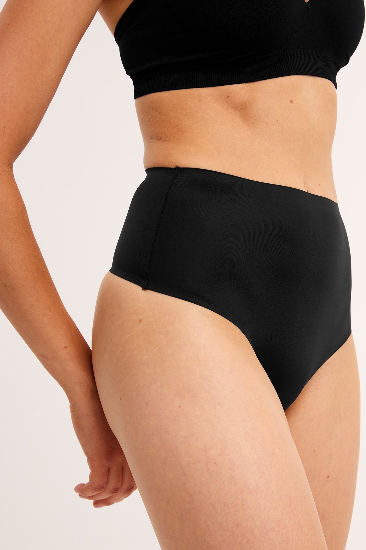 Naisen sivukuva mustissa korkeavyötäröisissä string-alushousuissa ja mustissa rintaliiveissä.