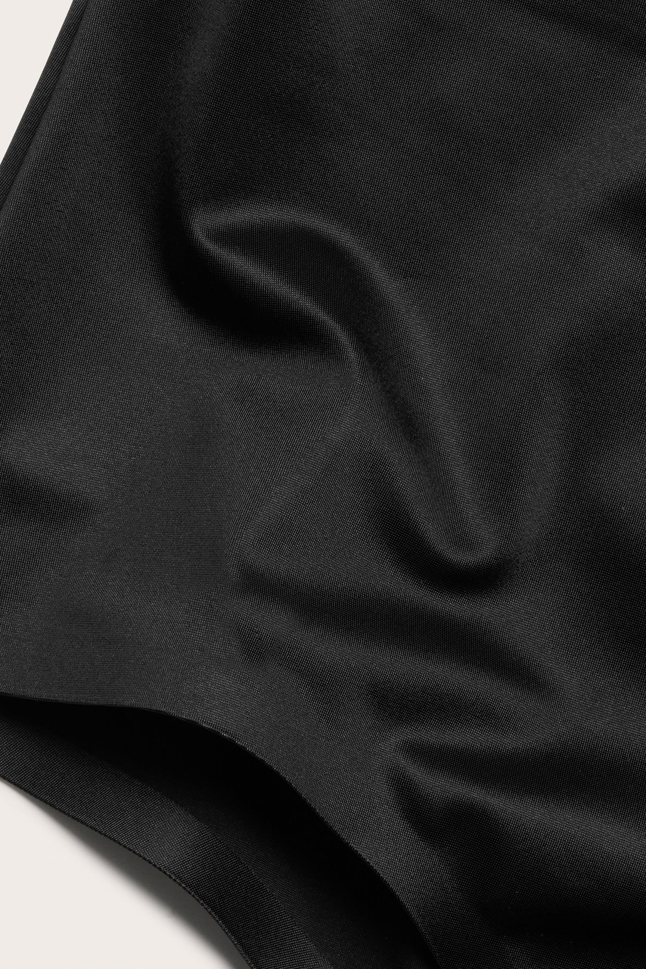 Zbliżenie czarnych stringów modelujących z gładkiej satynowej mikrofibry.