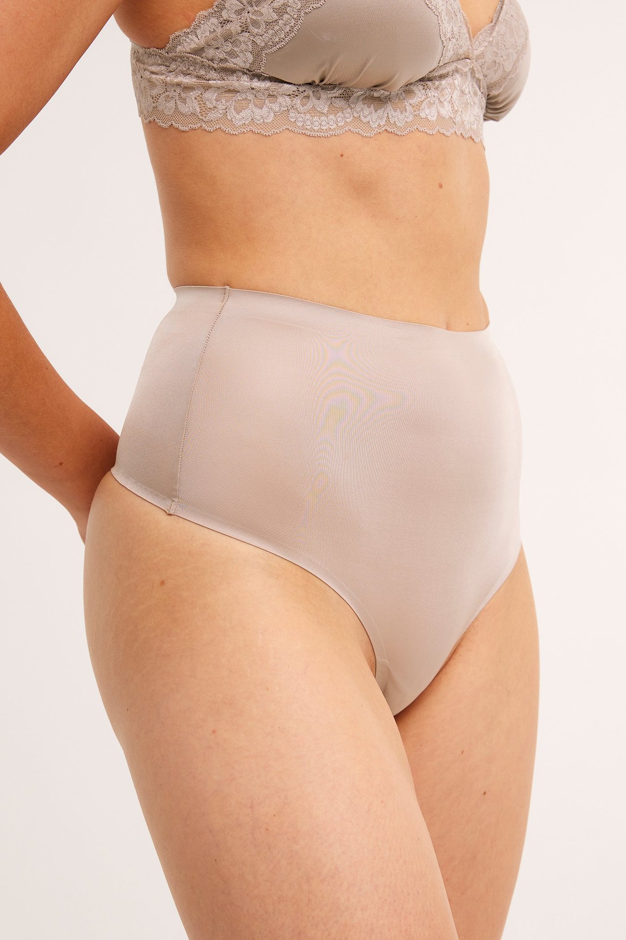 Sidebilde av en kvinne i lys rosa høy midje shaping stringtruse og matchende blonde-BH.