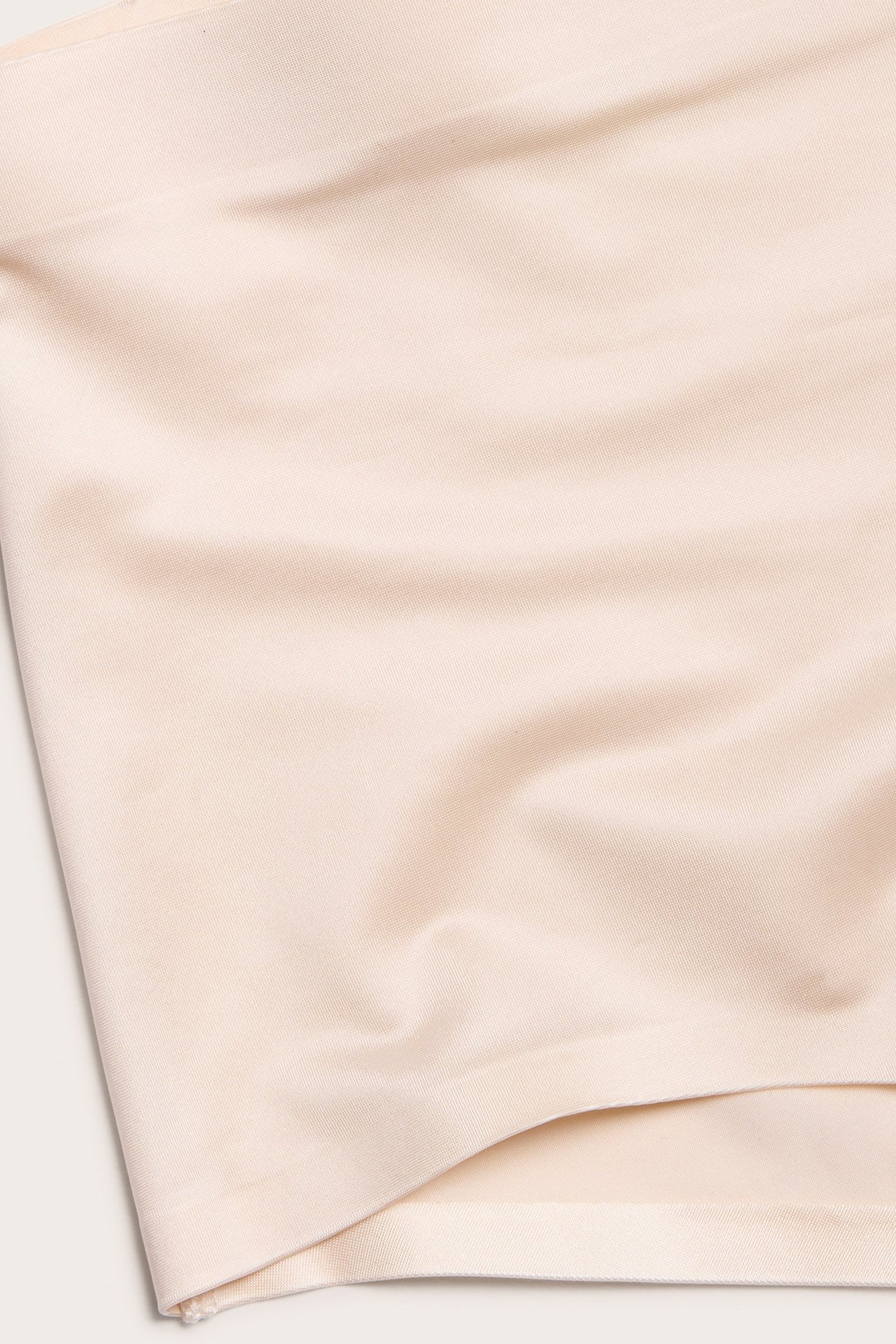 Zbliżenie beżowego, gładkiego materiału satynowo-mikrofibrowego, prawdopodobnie ze stringów modelujących.