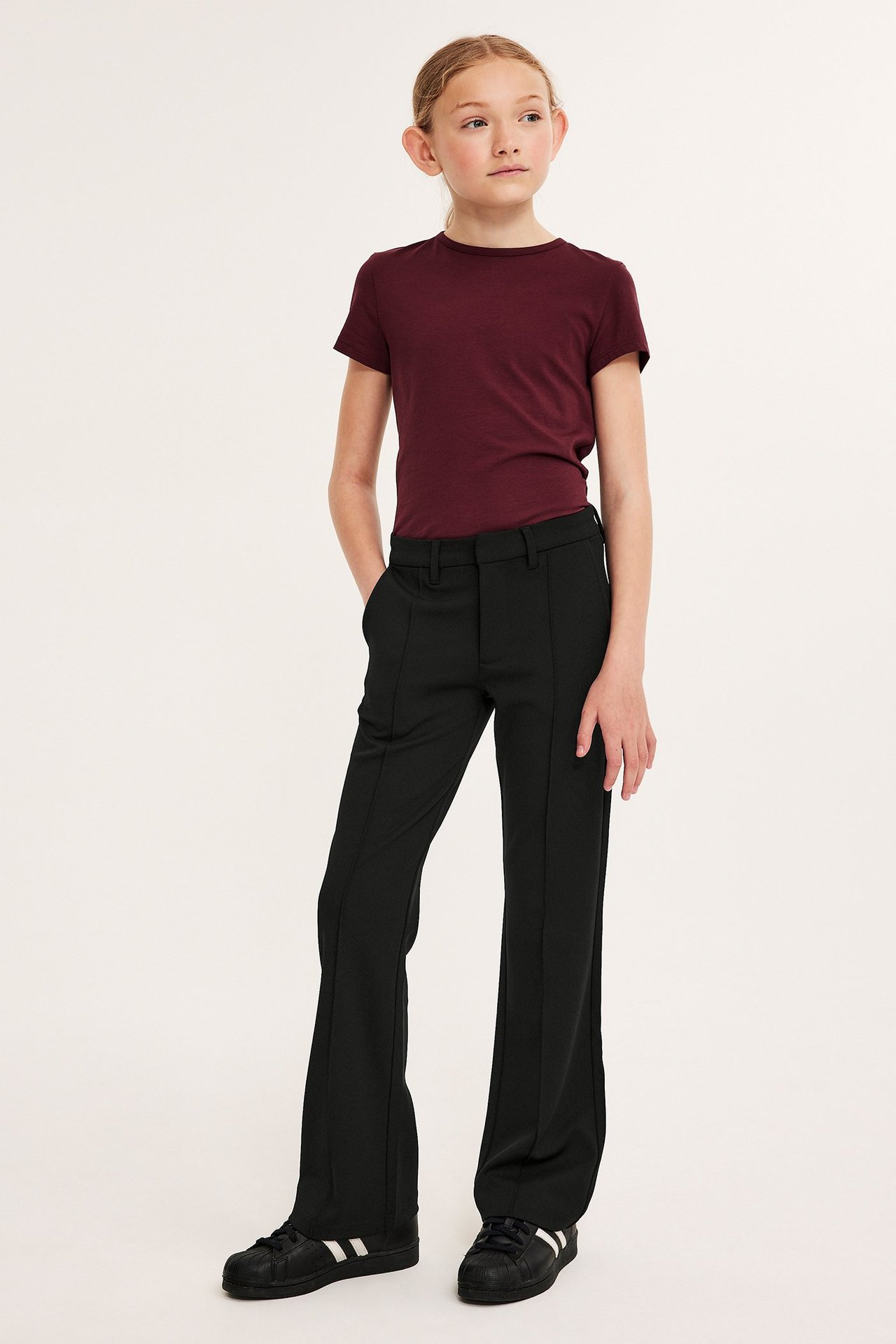 Frontbilde av en jente i svarte jersey flare-bukser med frontsømmer og en burgunder t-skjorte.