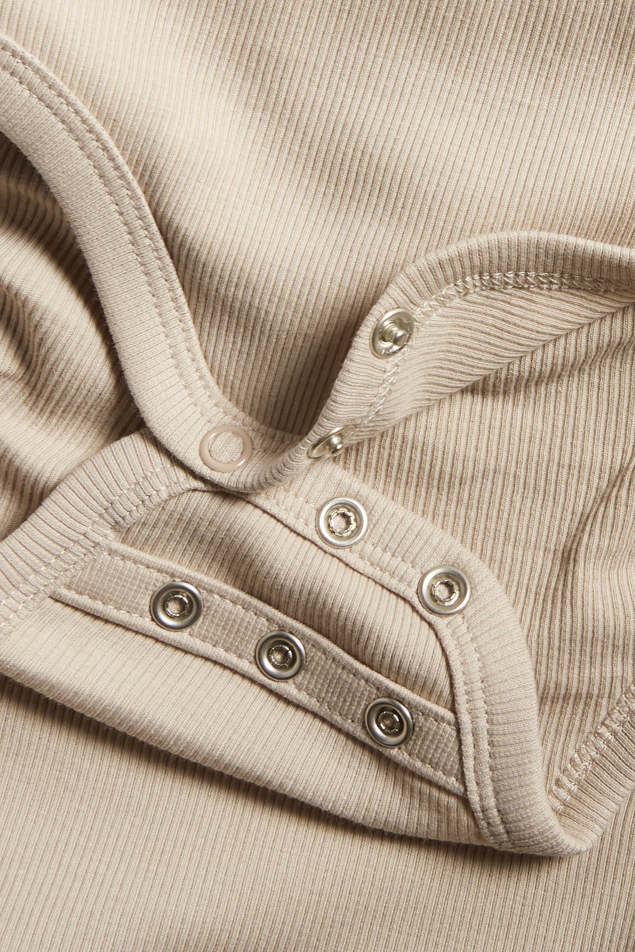 Zbliżenie beżowego prążkowanego body niemowlęcego z podwójnym rzędem zatrzasków w kroku.