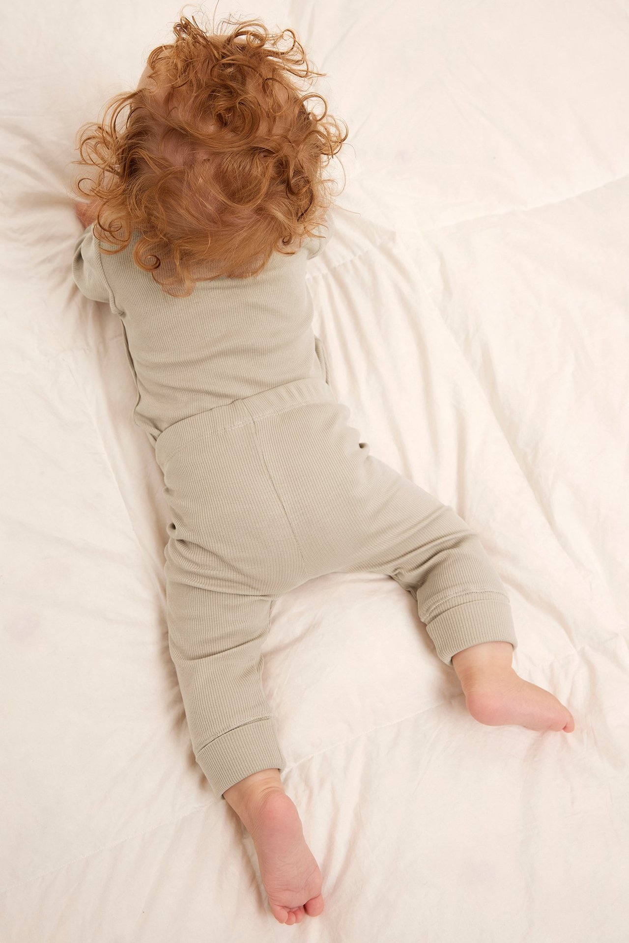 Uppifrån-vy av en baby i beiga ribbade leggings med muddar och matchande långärmad topp.