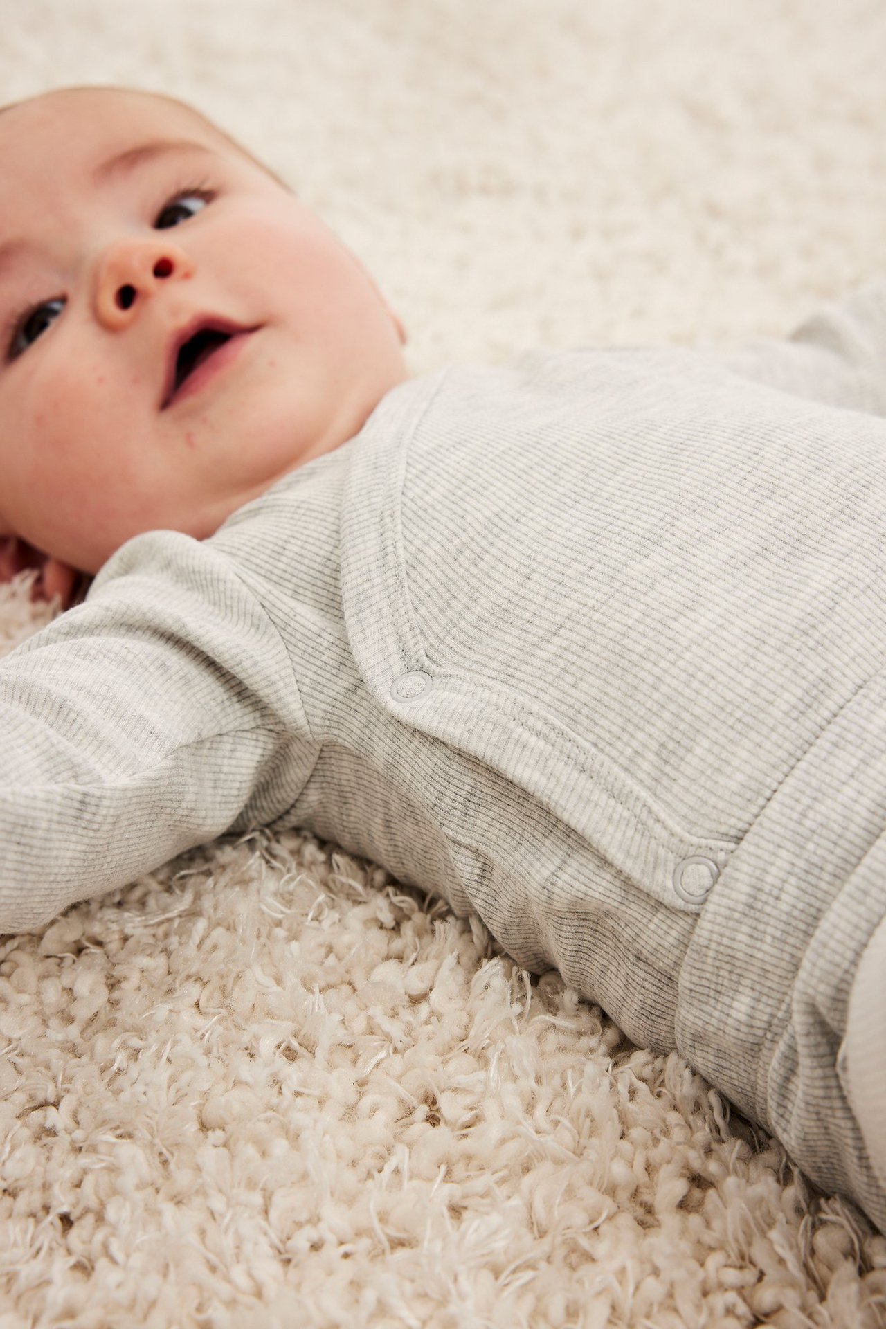 Zbliżenie dziecka w jasnoszarym prążkowanym body kopertowym z zatrzaskami.