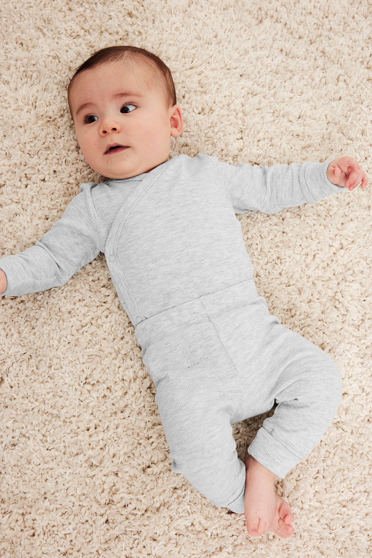 Uppifrån, baby i ljusgråmelerade ribbade leggings och matchande omlottbody.