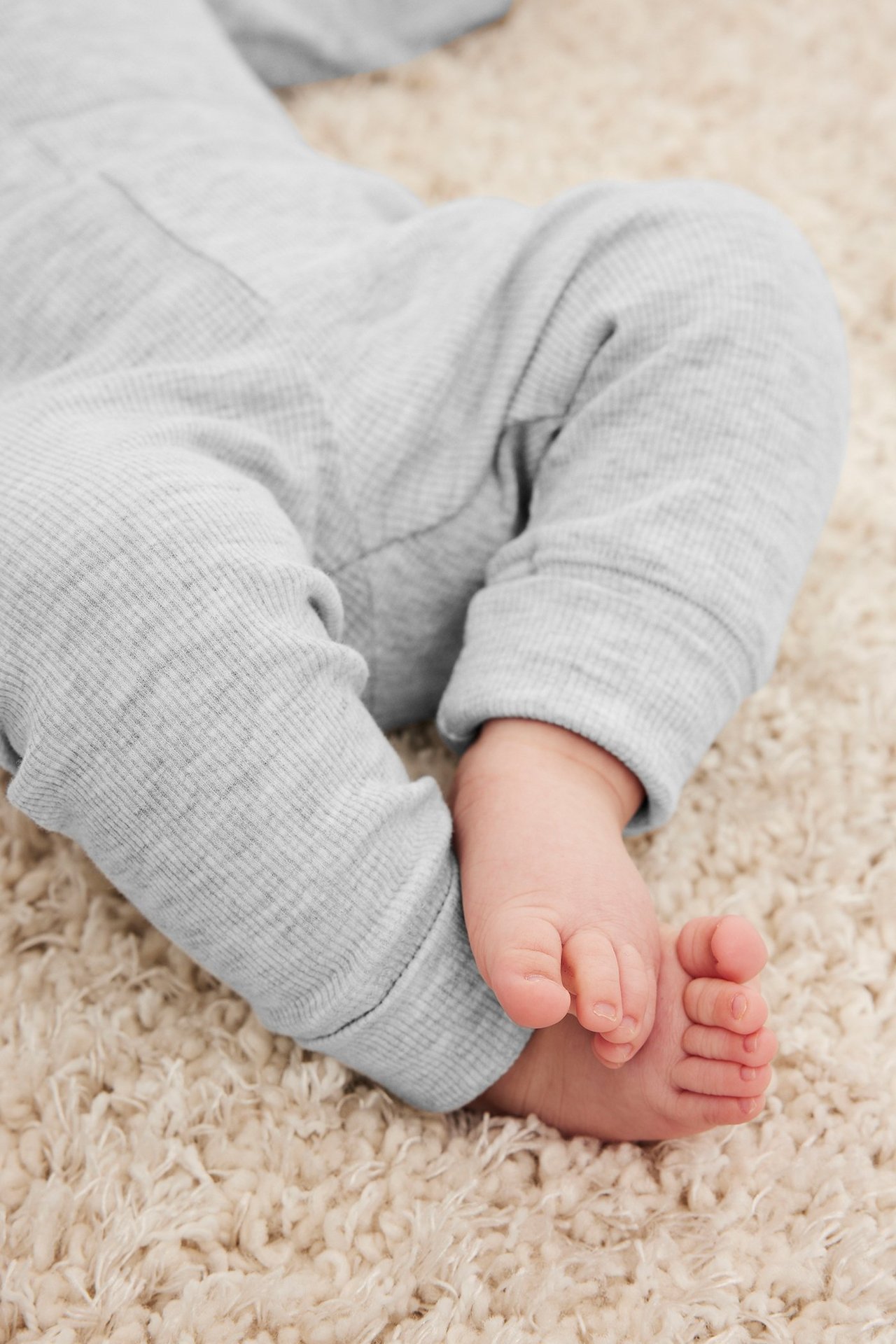 Lähikuva vauvan jaloista vaaleanharmaissa meleeratuissa ribbileggingseissä, joissa on leveät resorit.