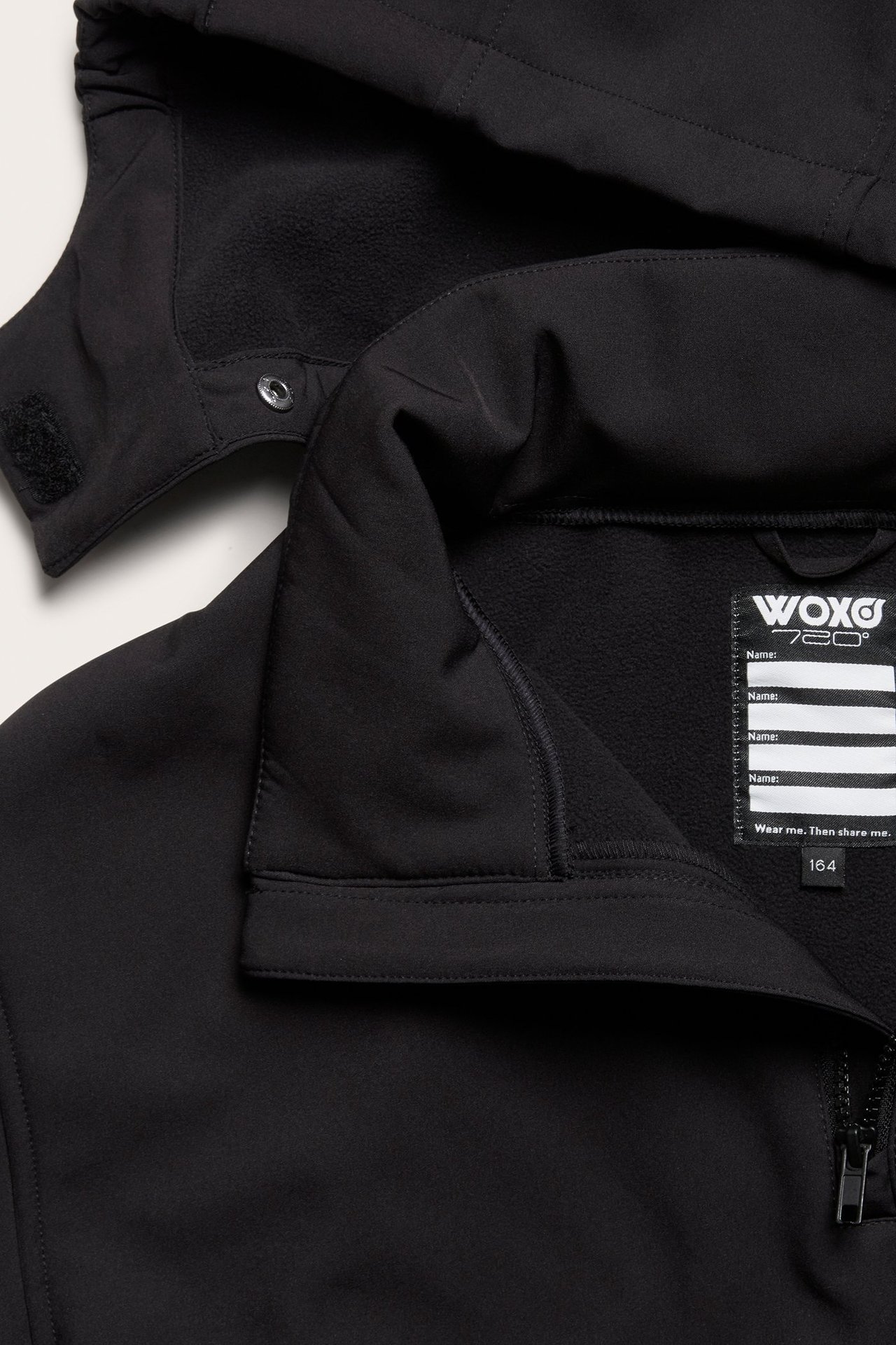 Zbliżenie czarnej kurtki softshell anorak z odpinanym kapturem, częściowym zamkiem błyskawicznym i polarową podszewką.