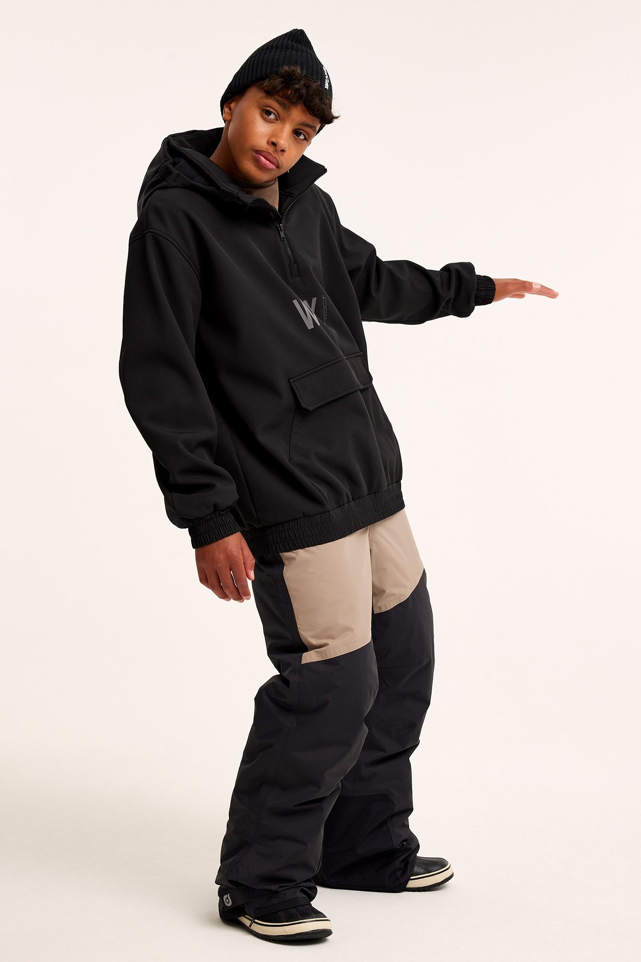 Widok z przodu: Dziecko w czarnej kurtce softshell, czarnej czapce, czarno-beżowych spodniach narciarskich i czarnych butach.