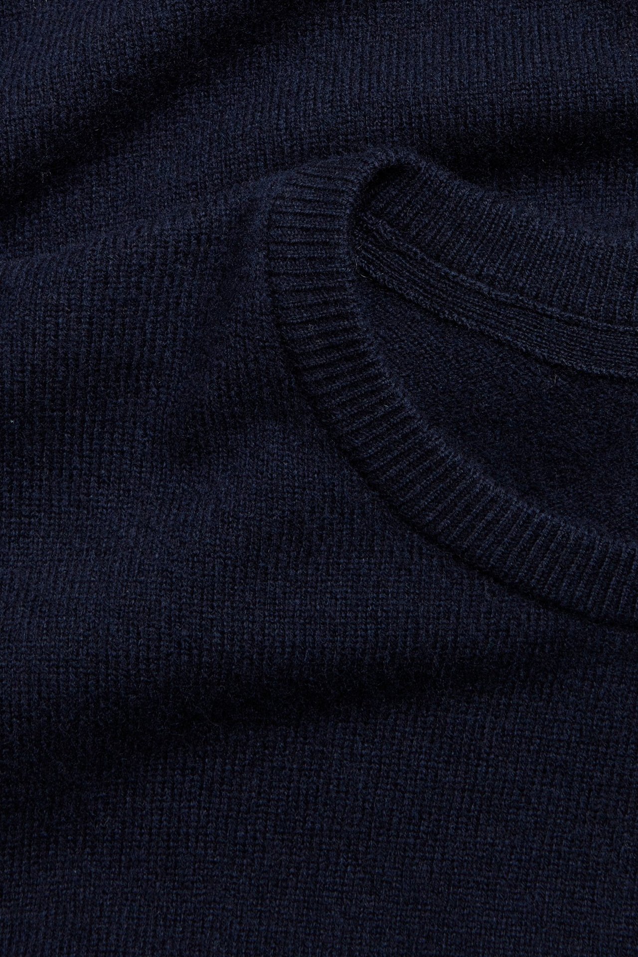 Zbliżenie na ciemnoniebieski, jednolity sweter wełniany z okrągłym dekoltem i prążkowanymi detalami.