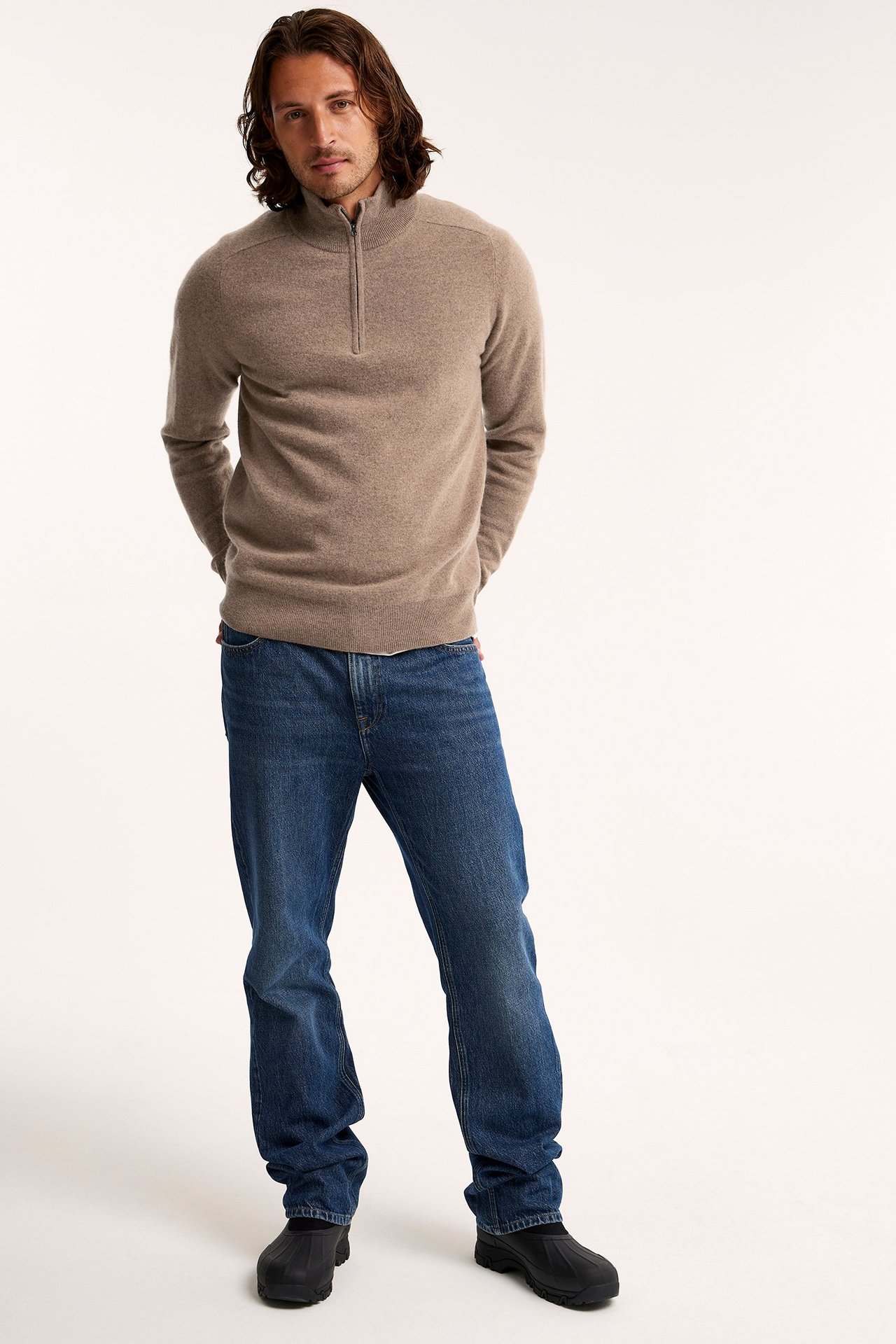 Forfra: mann i brunmelert half-zip ullgenser, blå jeans og svarte sko.
